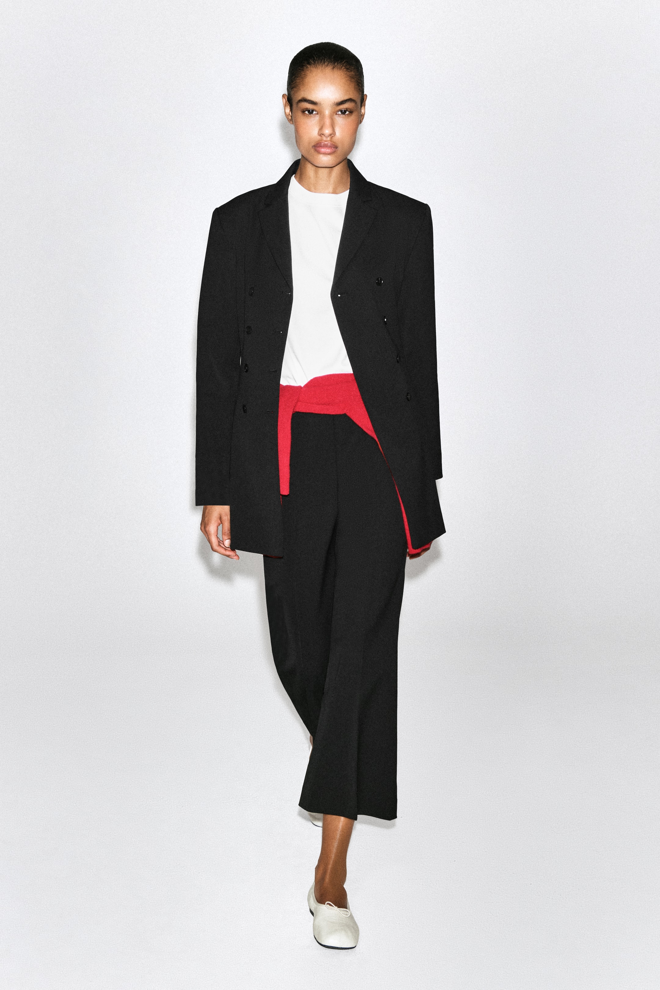 Ver imagen más grande: Se muestra un par de pantalones negros cropped acampanados desde el frente, con un corte ajustado en el muslo que se abre ligeramente hasta un bajo cropped que termina por encima del tobillo. Los pantalones se combinan con un jersey rojo atado a la cintura, que define la silueta de tiro alto.