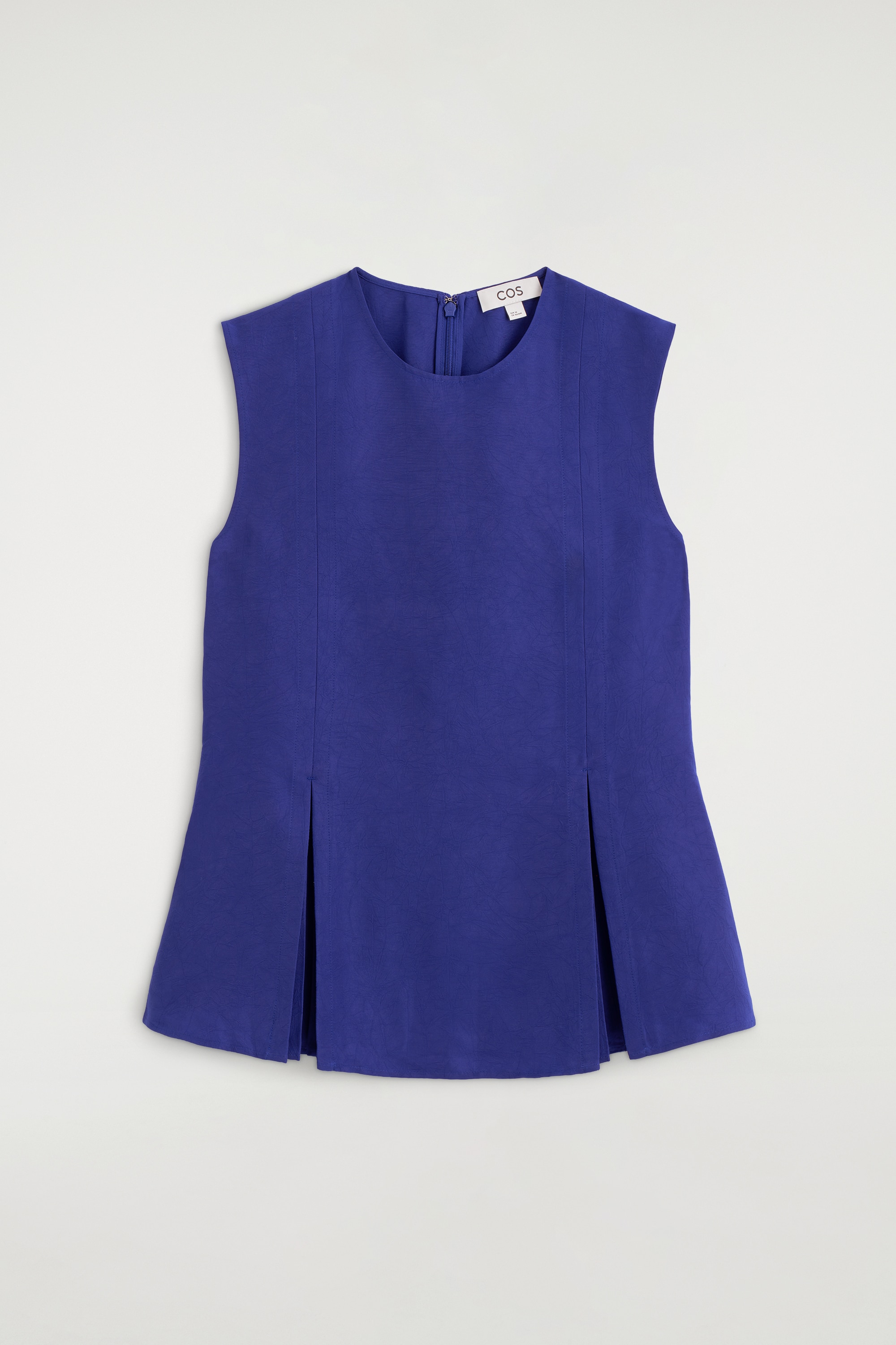 Un vivace top peplum blu senza maniche Ã¨ mostrato frontalmente, con girocollo e pieghe verticali strutturate che si aprono sullâorlo. Il top Ã¨ abbinato a pantaloni neri dalla vestibilitÃ  rilassata, mettendo in risalto la sua silhouette svasata.