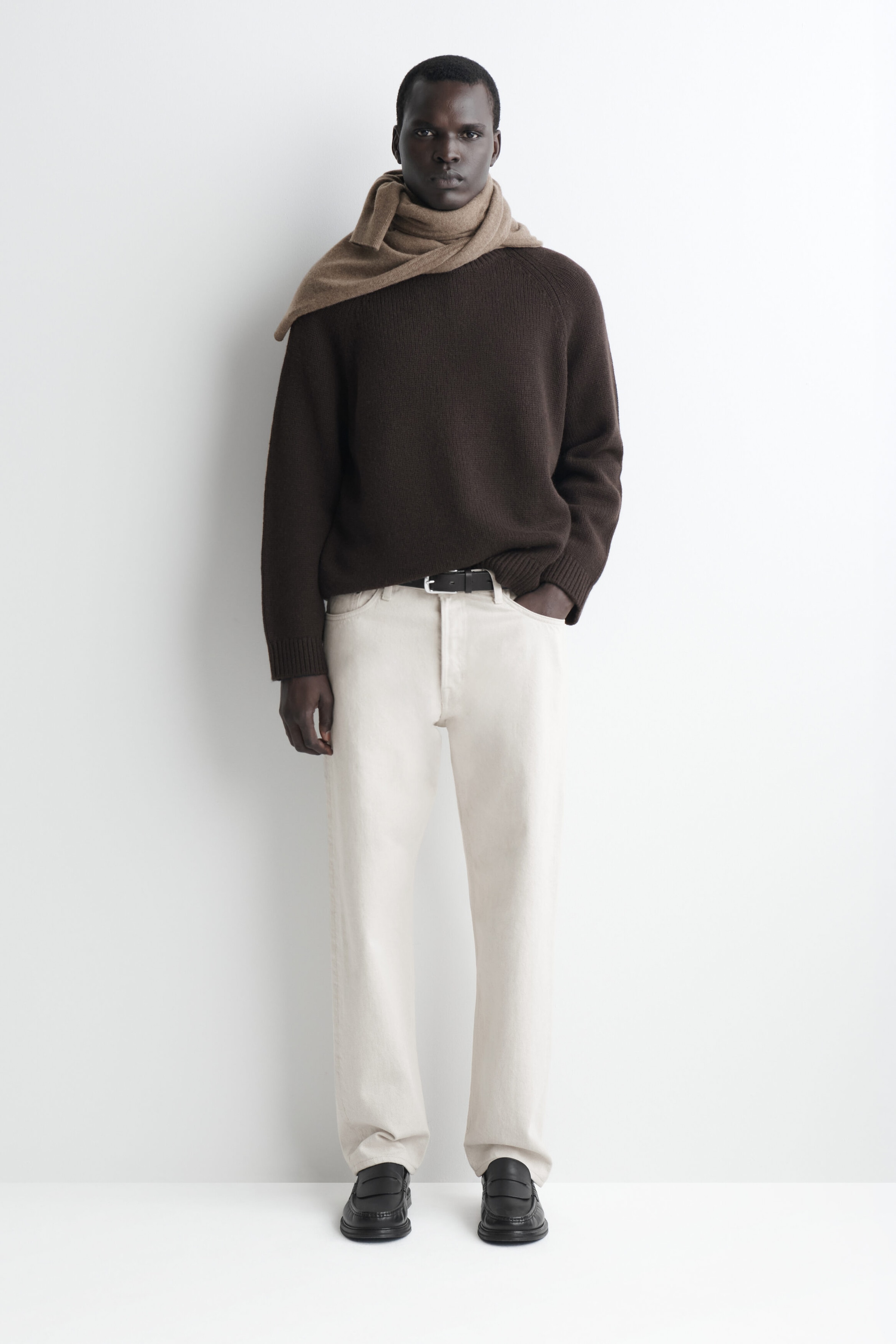 The dark brown chunky cashmere sweater is shown from the front, featuring a relaxed fit, raglan sleeves, and ribbed cuffs. It is styled with a beige knit scarf draped around the neck and shoulders, with the hem slightly tucked into cream-coloured trousers. The dark brown chunky cashmere sweater is shown from the front, featuring a relaxed fit, raglan sleeves, and ribbed cuffs. It is styled with a beige knit scarf draped around the neck and shoulders, with the hem slightly tucked into cream-coloured trousers.