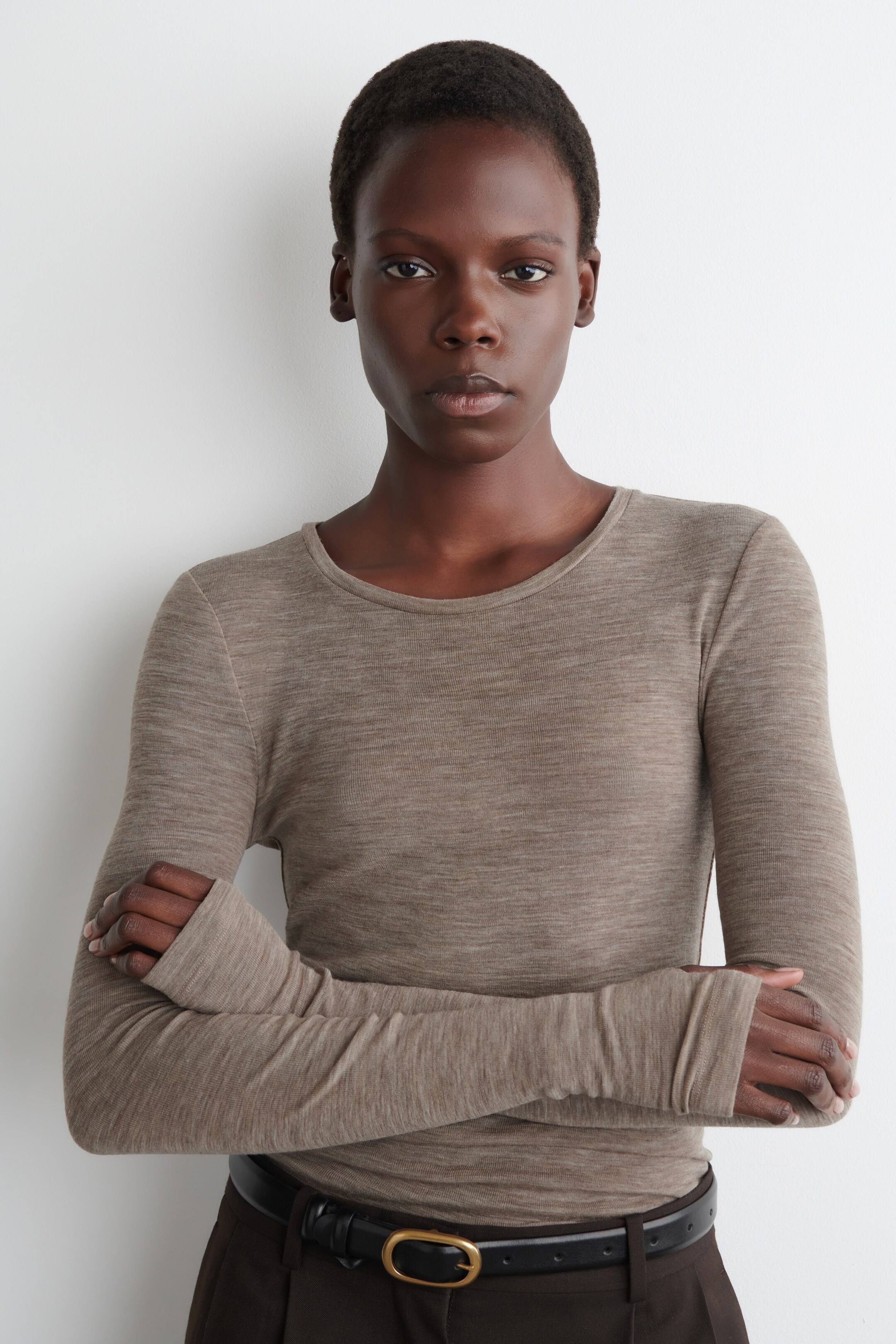 View larger image: A light brown marl, long-sleeved top is being worn, featuring a scoop neckline and form-fitting sleeves with thumbholes. The top is presenting a front-facing view, tucked into dark brown trousers with a black belt and gold buckle, highlighting its slim fit.