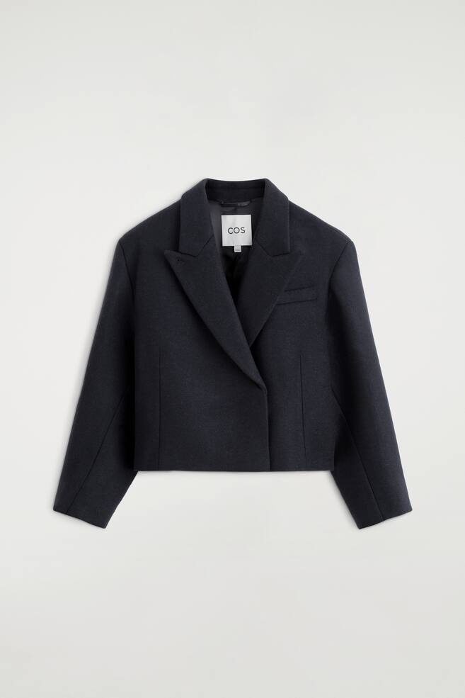 Ein oversized, verkÃ¼rzter Blazer aus einer gekochten Wollmischung wird von vorne gezeigt und verfÃ¼gt Ã¼ber eine kastige Silhouette mit breiten Reverskragen und asymmetrischem, Ã¼berkreuztem Frontverschluss. Dieser marineblaue Blazer zeigt lange, weite Ãrmel, eine einzelne Brustleistentasche und einen klaren, geraden Saum. - 1