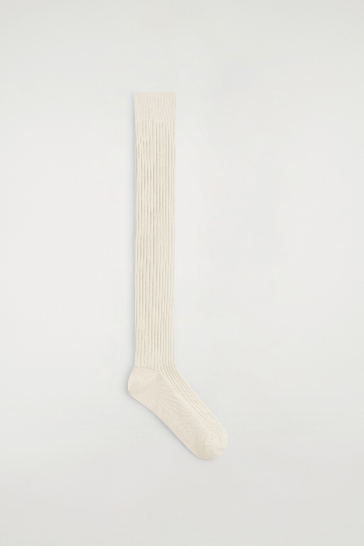 A long wool boot sock in an off-white color is lying flat in side profile, showcasing its extra-long length and vertical ribbed knit texture. The sock features a ribbed cuff at the top and smooth, solid-knit panels at the heel and toe.