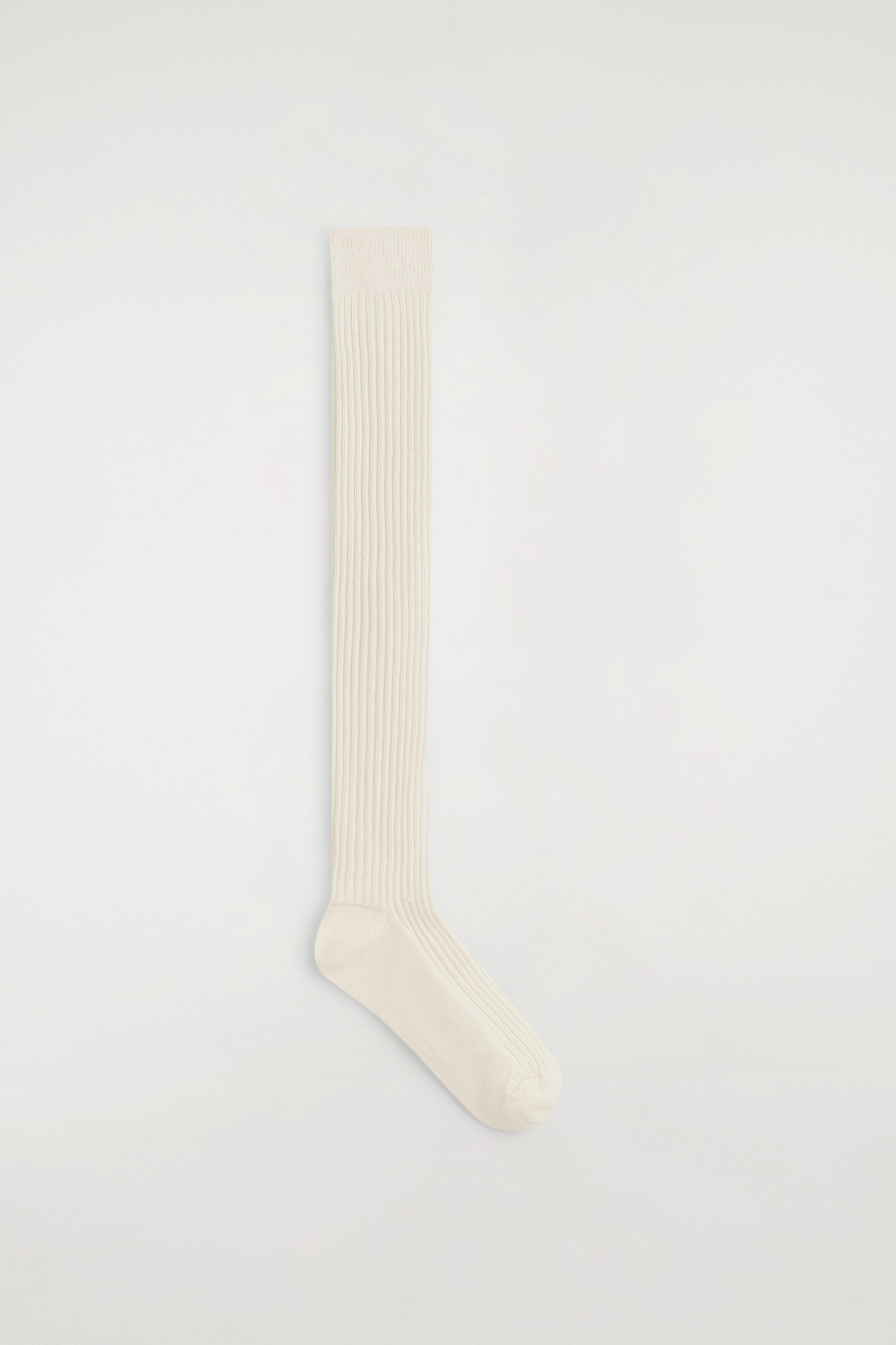 A long wool boot sock in an off-white color is lying flat in side profile, showcasing its extra-long length and vertical ribbed knit texture. The sock features a ribbed cuff at the top and smooth, solid-knit panels at the heel and toe. A long wool boot sock in an off-white color is lying flat in side profile, showcasing its extra-long length and vertical ribbed knit texture. The sock features a ribbed cuff at the top and smooth, solid-knit panels at the heel and toe.