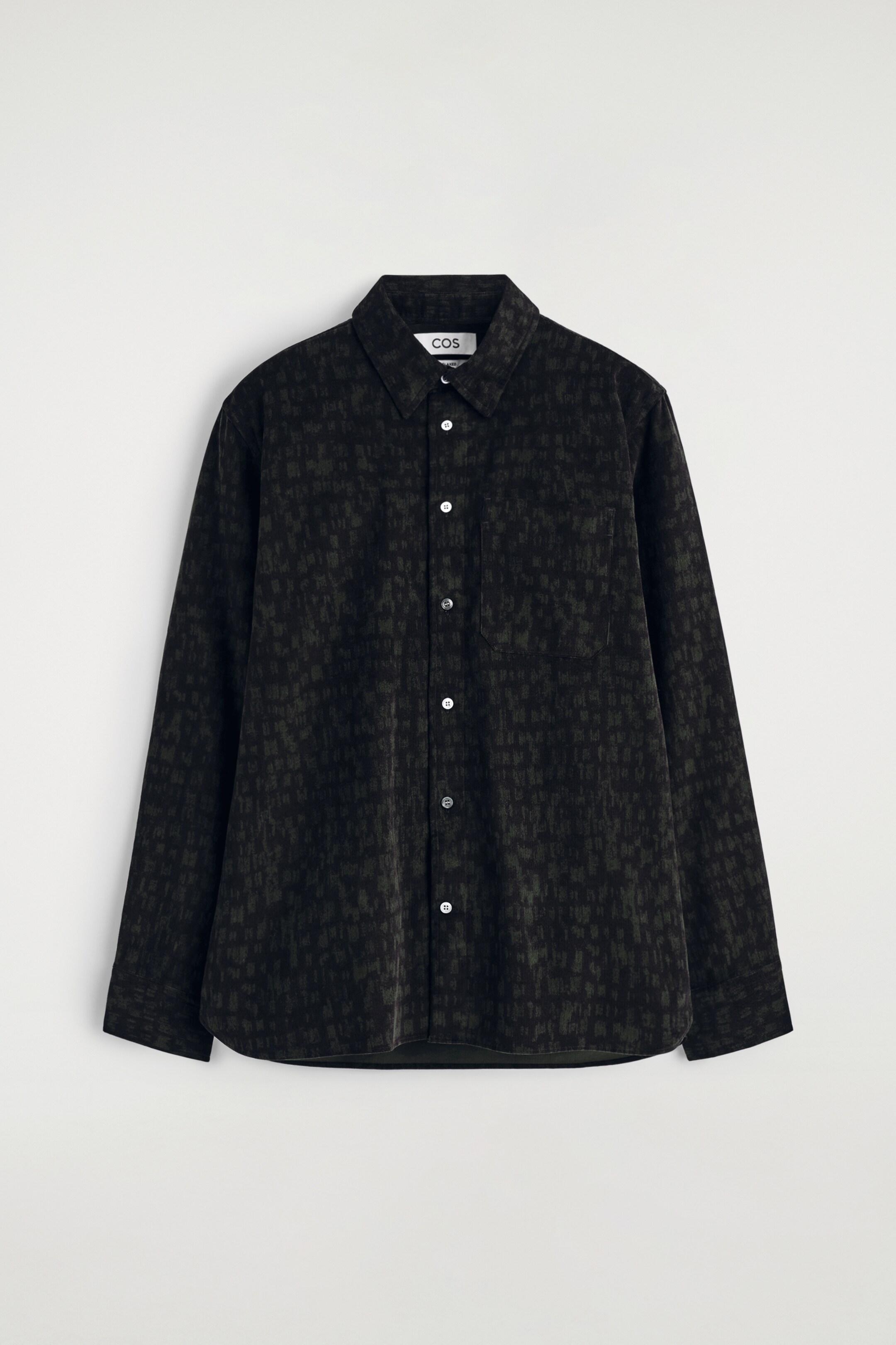 Agrandir l'image: La chemise en velours côtelé est présentée de face et à plat, avec un motif abstrait vert foncé et noir et une texture à fines côtes visible. Elle est conçue avec un col standard, une fermeture à boutons sur le devant avec des boutons en nacre blanche, une poche poitrine unique à gauche et des manches longues, affichant une coupe décontractée et un ourlet subtilement incurvé.
