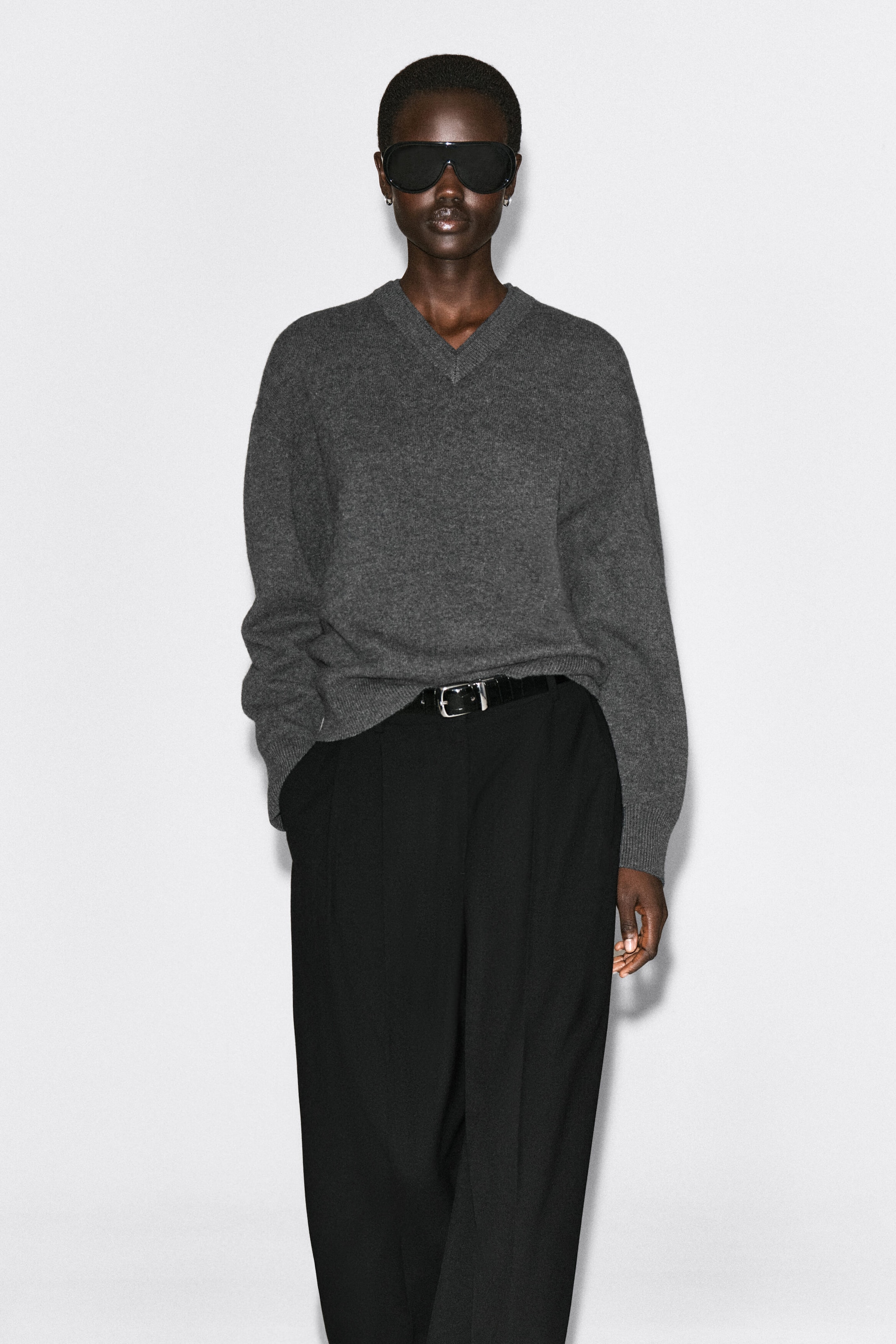 The gray merino wool layered V-neck sweater is shown from the front, featuring a relaxed-fit silhouette with a double-layered ribbed V-neckline, dropped shoulders, and ribbed cuffs. It drapes softly over the body and is styled with a partial tuck into black trousers to highlight its lightweight texture. The gray merino wool layered V-neck sweater is shown from the front, featuring a relaxed-fit silhouette with a double-layered ribbed V-neckline, dropped shoulders, and ribbed cuffs. It drapes softly over the body and is styled with a partial tuck into black trousers to highlight its lightweight texture.