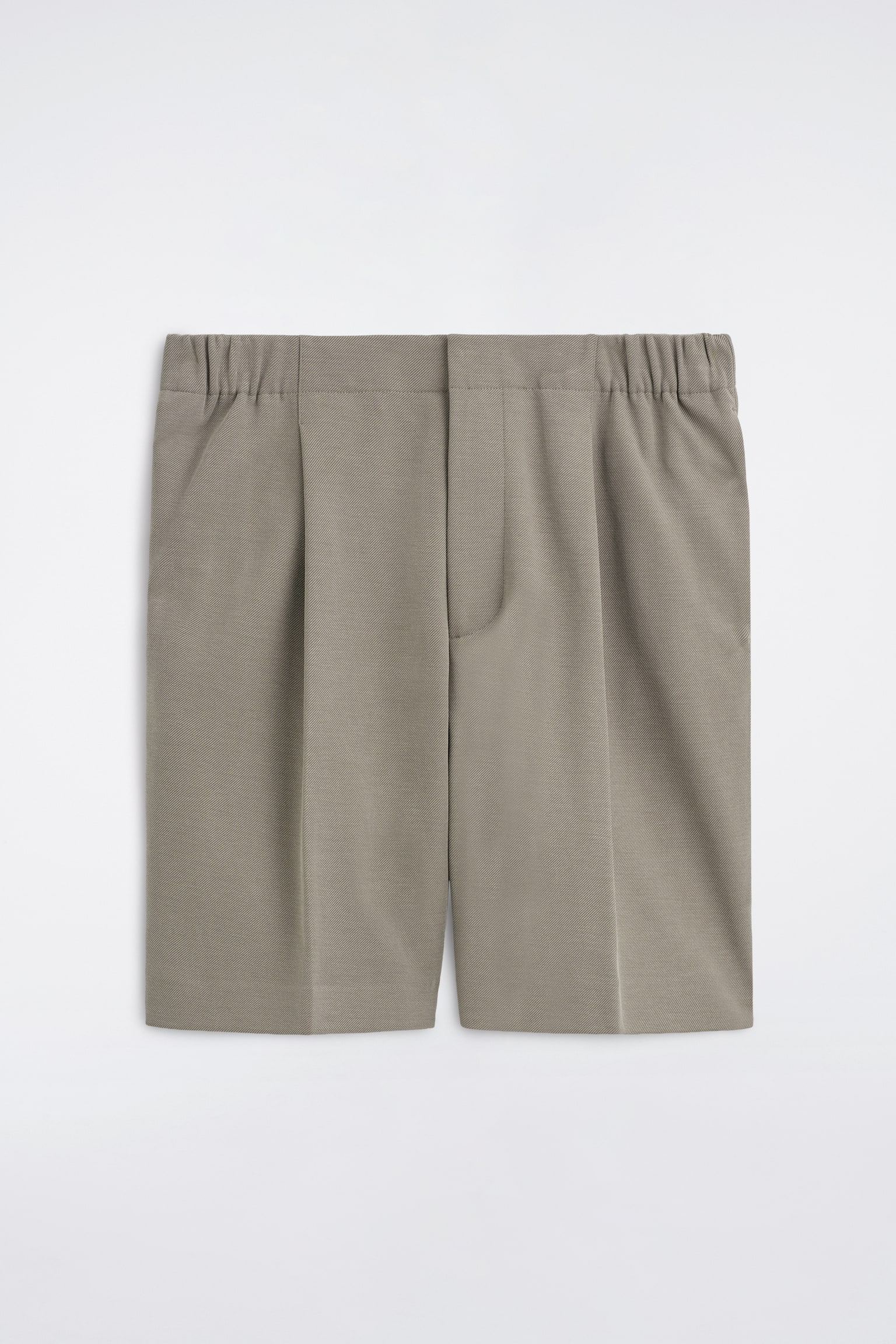 I Tailored Bonded-Twill Shorts sono mostrati in vista frontale, mettendo in evidenza un tessuto strutturato color taupe-grigio con cintura anteriore piatta e inserti laterali elasticizzati. Gli shorts presentano pince singole che sfumano in pieghe centrali nette lungo le gambe, oltre a tasche laterali e una patta anteriore nascosta.