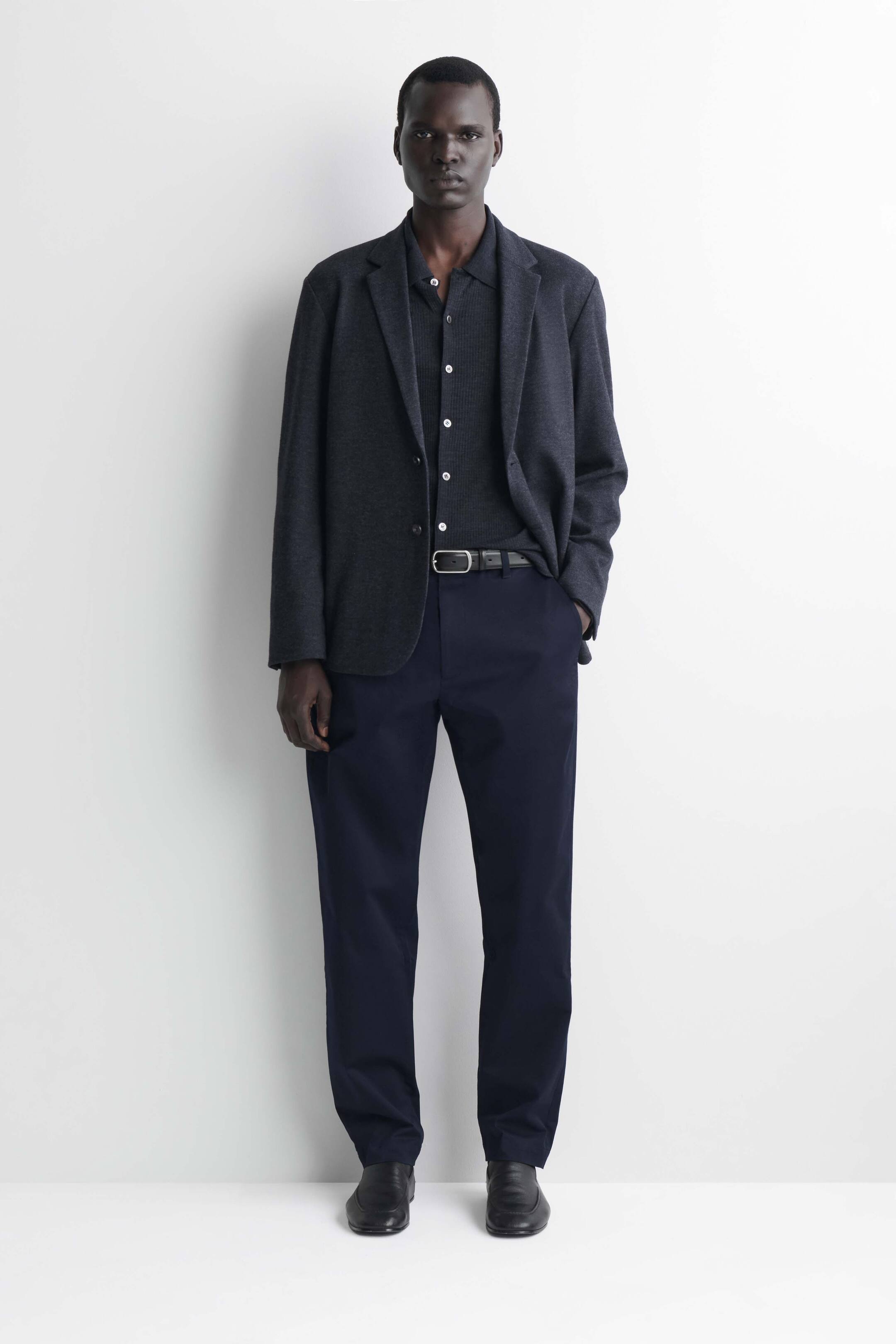 Grotere afbeelding bekijken: Marineblauwe katoenen chino's met slim fit en rechte pijp worden van voren getoond, gestyled met een zwarte leren riem in de taille. De broek valt in een strakke, gestructureerde rechte pijp en rust netjes op zwarte leren schoenen.