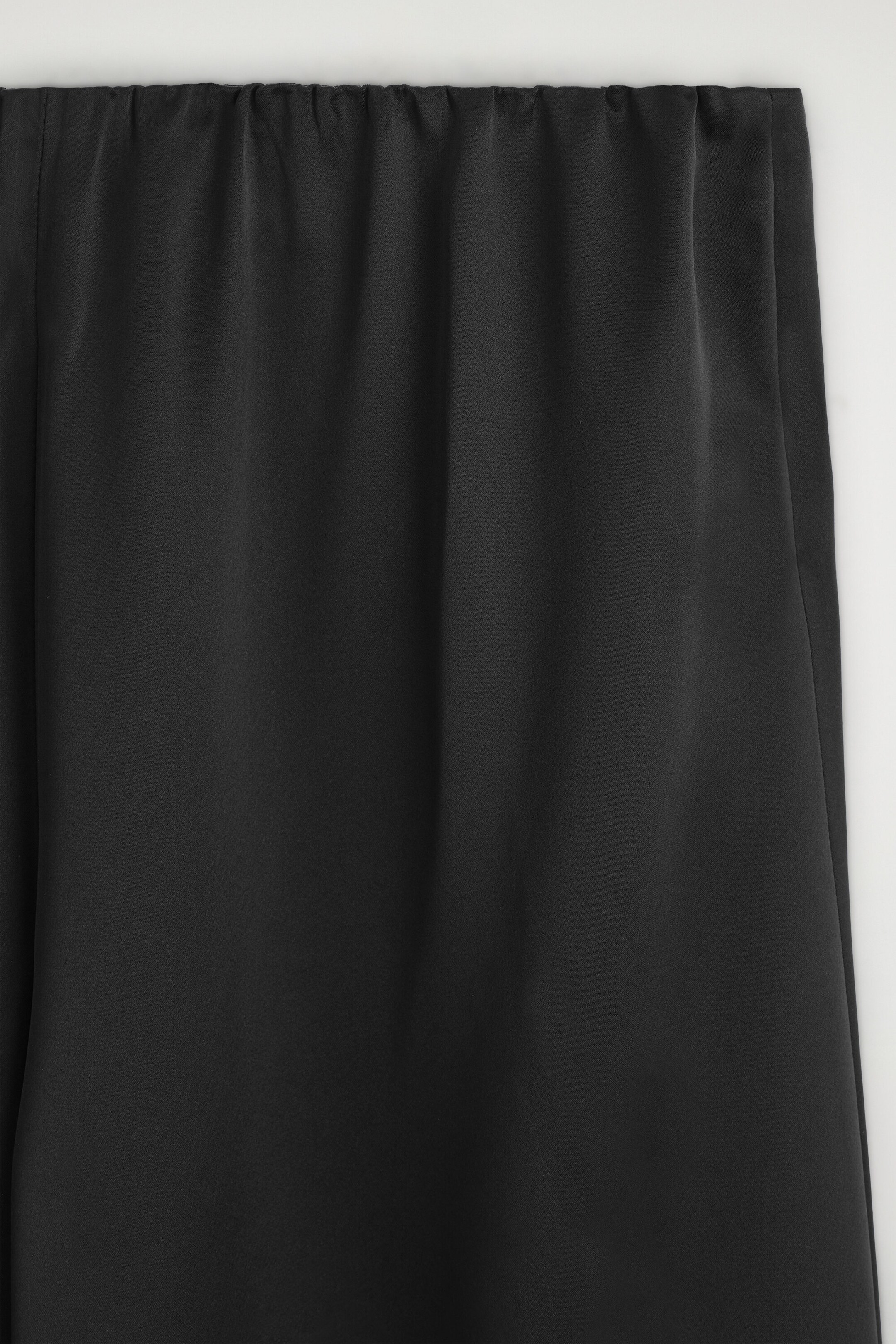 Black satin pants are shown in a close-up front view, highlighting the gathered elastic waistband and the smooth, lustrous fabric draping down. Black satin pants are shown in a close-up front view, highlighting the gathered elastic waistband and the smooth, lustrous fabric draping down.
