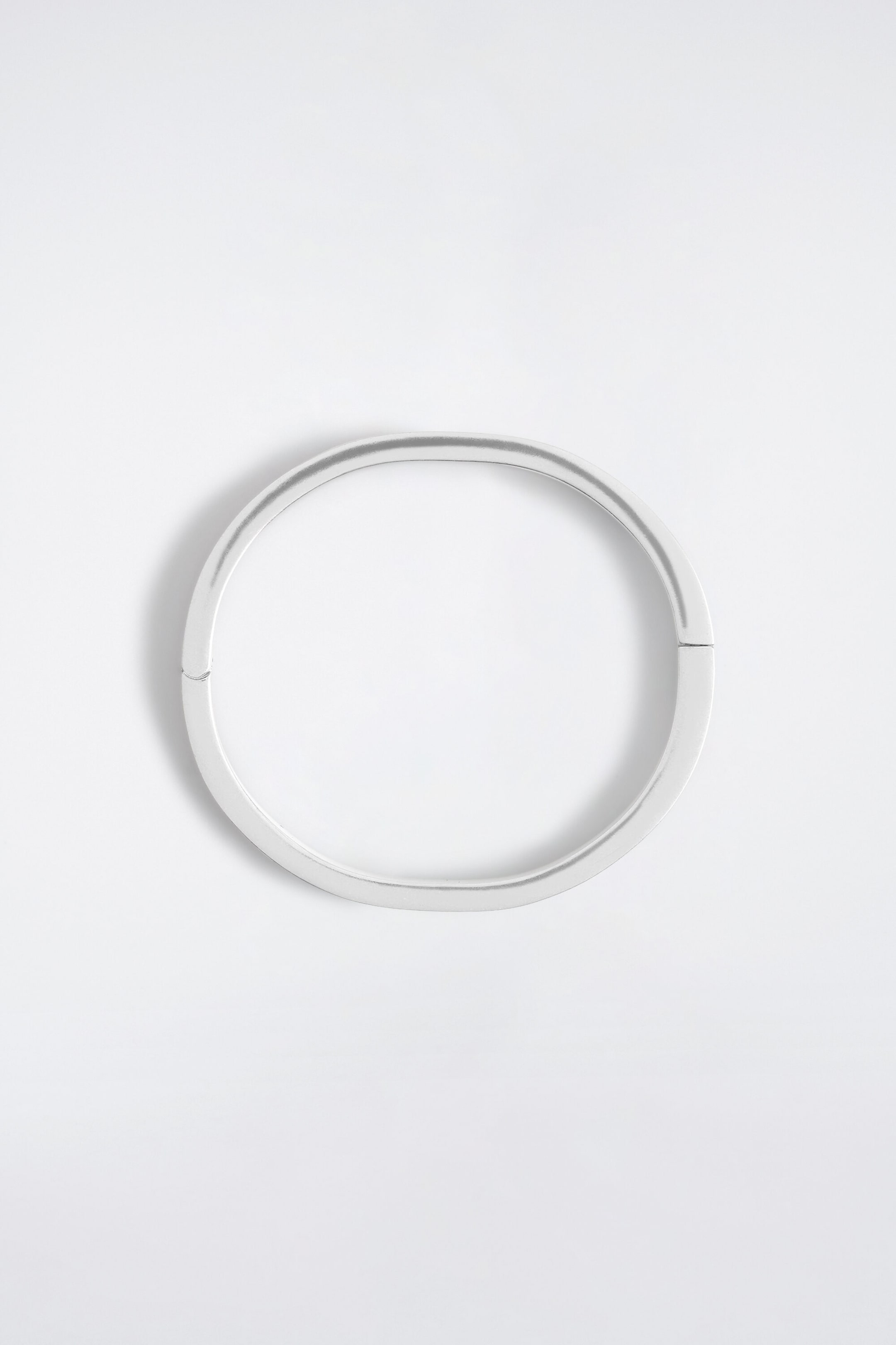 Un bracelet jonc minimaliste ton argent est posé à plat, mettant en valeur son design ovale aux lignes épurées et sa finition métallique brossée. La pièce est dotée d’un fermoir à charnière, visible par les petites jonctions de chaque côté. Un bracelet jonc minimaliste ton argent est posé à plat, mettant en valeur son design ovale aux lignes épurées et sa finition métallique brossée. La pièce est dotée d’un fermoir à charnière, visible par les petites jonctions de chaque côté.