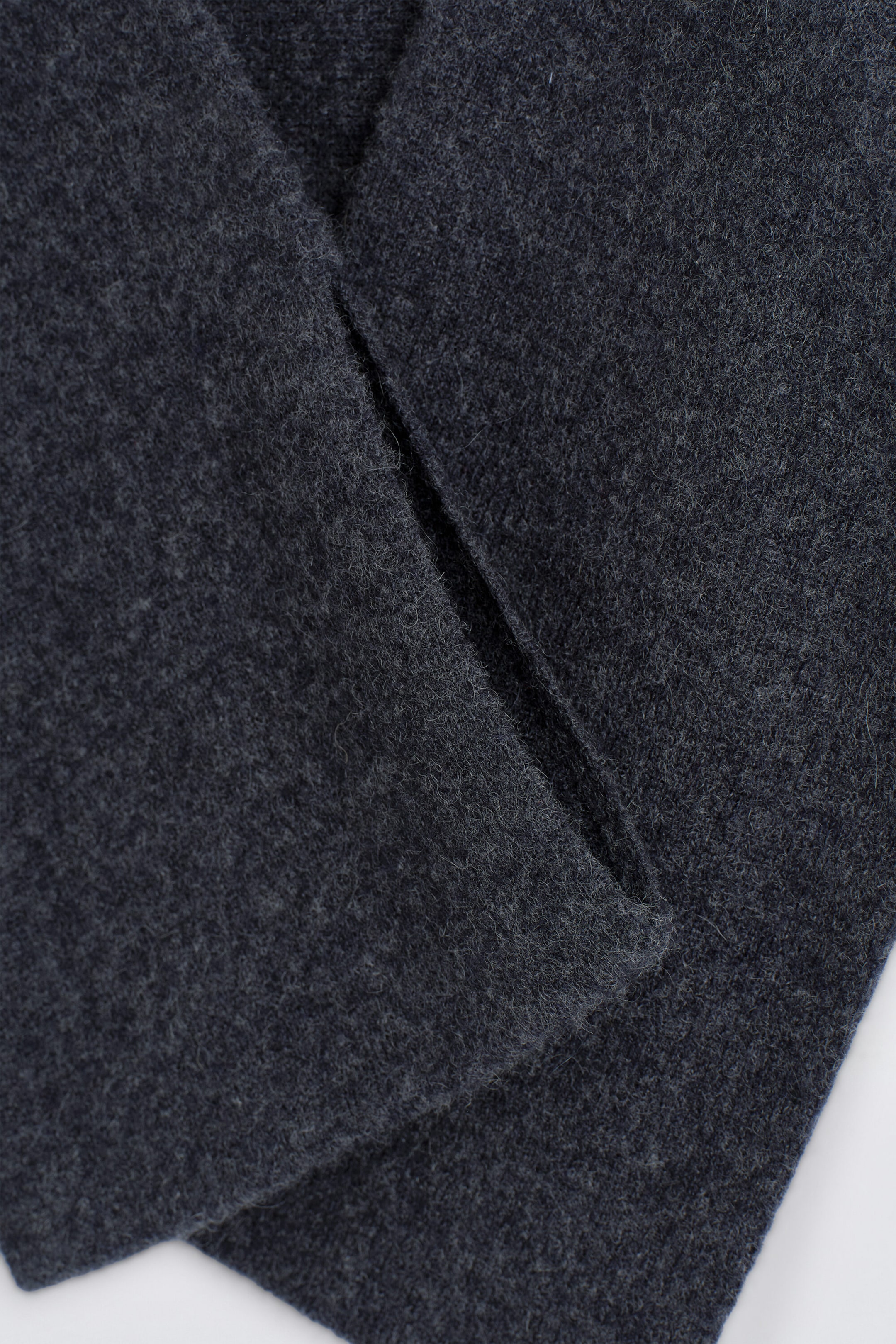 The cashmere pull-through scarf is shown in a close-up detail of its soft, dark gray knit fabric. One end of the scarf is threaded through the integrated vertical slit to demonstrate the pull-through design. The cashmere pull-through scarf is shown in a close-up detail of its soft, dark gray knit fabric. One end of the scarf is threaded through the integrated vertical slit to demonstrate the pull-through design.