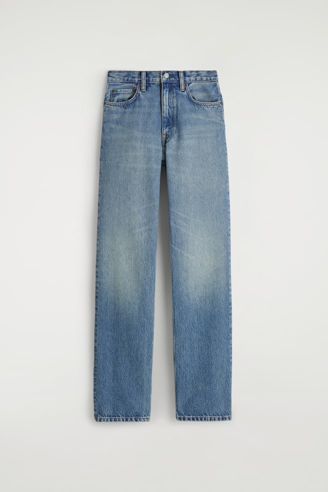 Une paire de jeans en denim bleu est présentée de face, avec une coupe droite et une taille haute. Le jean présente une teinte bleu clair délavé avec un dégradé naturel sur les cuisses et les genoux, et est détaillé avec des poches avant en forme de cuillère, une fermeture à bouton et à glissière, et des surpiqûres couleur tabac. - 1