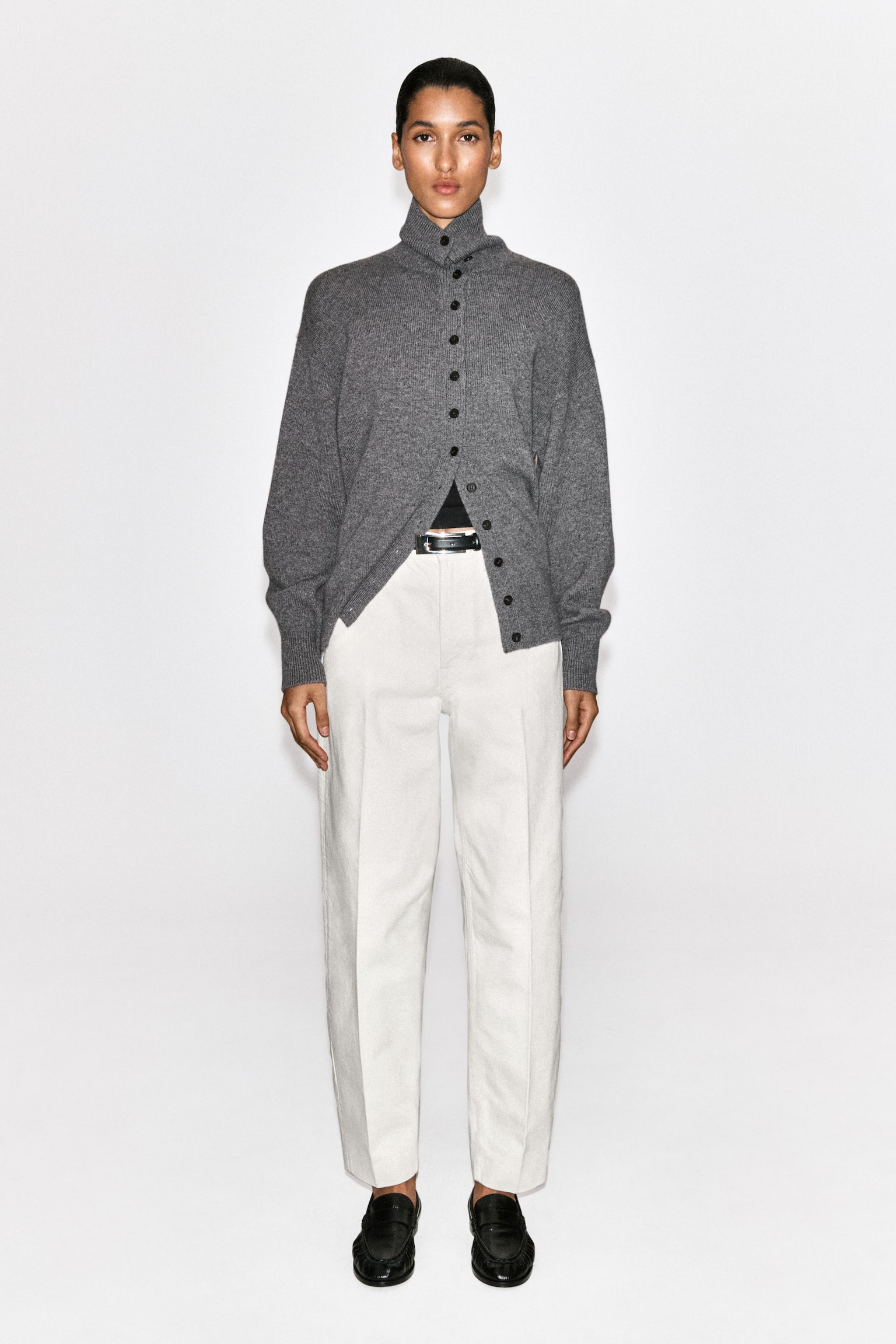 Un pantalon de couleur crème est présenté de face, avec une ceinture dotée de passants pour ceinture et une fermeture à bouton unique. Deux poches avant, dont une poche à monnaie, sont visibles avec des rivets en métal, et les jambes droites se terminent par des ourlets finis. - 1