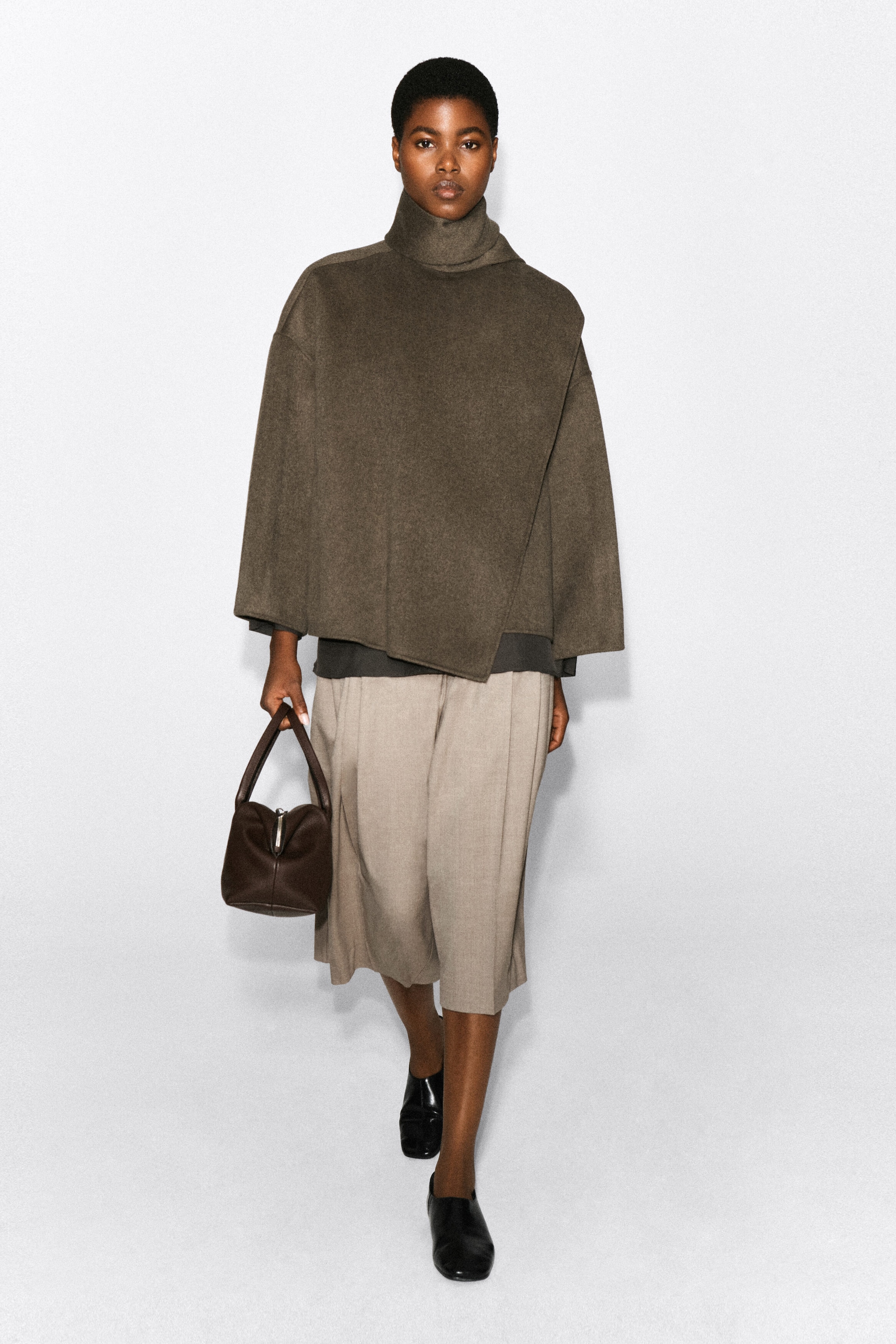 A double-faced wool-blend scarf jacket in dark olive-brown is being worn by the model, featuring a high, draped scarf collar and a relaxed, wide-sleeve silhouette. The jacket is styled with light beige wide-leg cropped trousers, black leather shoes, and a small dark brown handbag. A double-faced wool-blend scarf jacket in dark olive-brown is being worn by the model, featuring a high, draped scarf collar and a relaxed, wide-sleeve silhouette. The jacket is styled with light beige wide-leg cropped trousers, black leather shoes, and a small dark brown handbag.