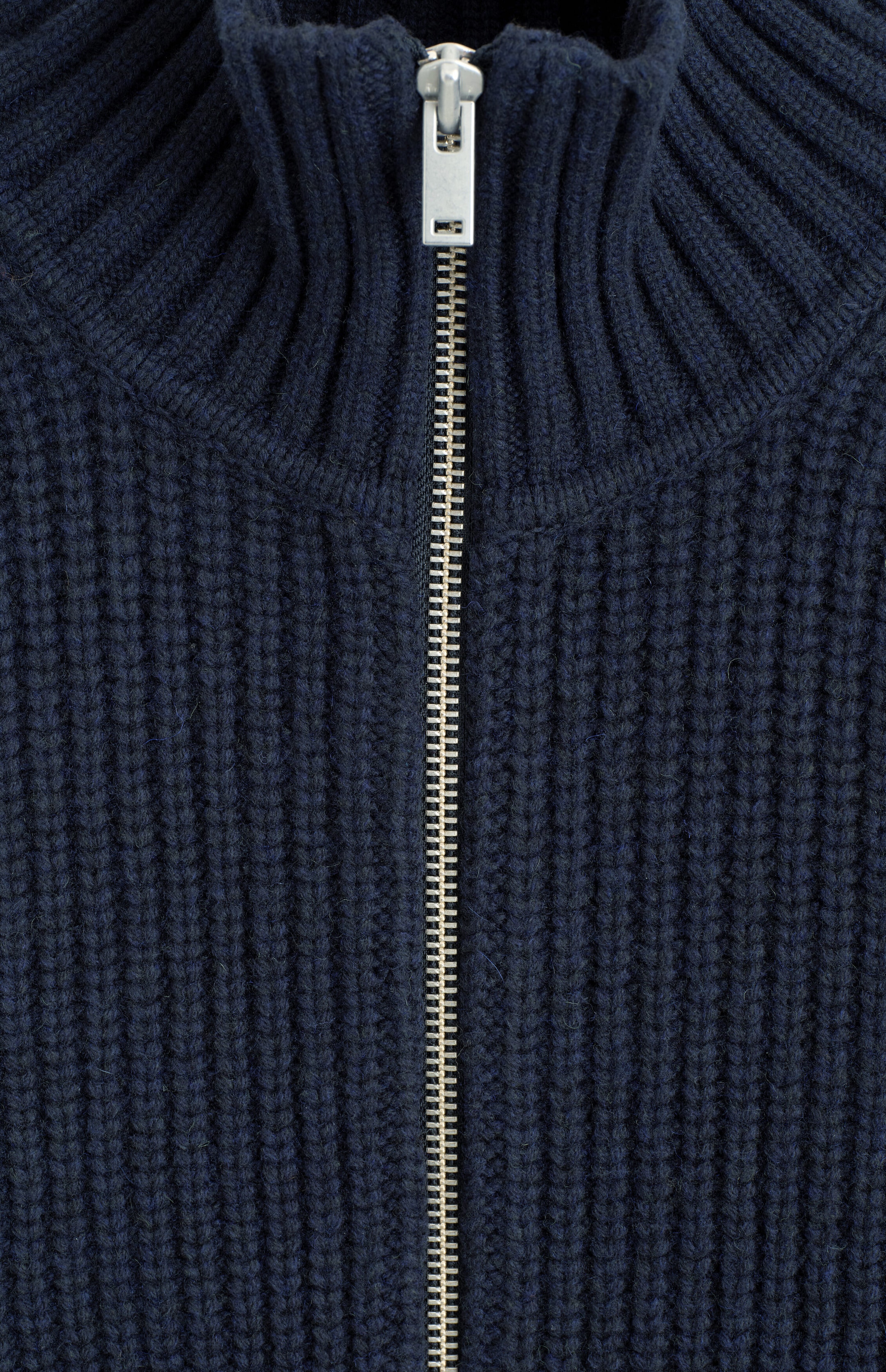 A navy blue ribbed-knit sweater is shown in a close-up front view, featuring a high ribbed mock neck collar and a silver-tone metal zipper running down the center. A navy blue ribbed-knit sweater is shown in a close-up front view, featuring a high ribbed mock neck collar and a silver-tone metal zipper running down the center.