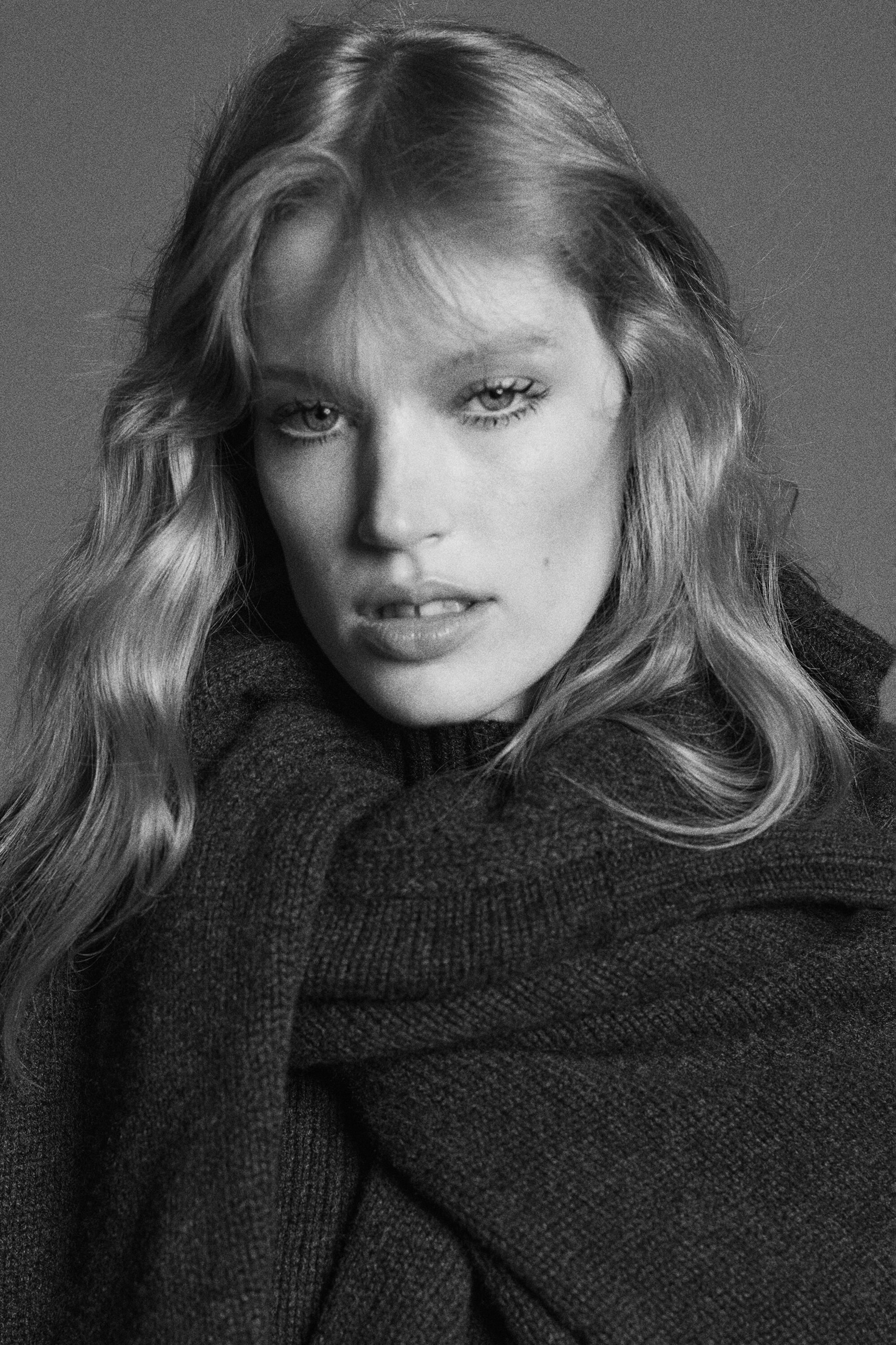 The chunky cashmere funnel-neck jumper is shown in a close-up, front-facing black-and-white portrait. It features a high ribbed collar and a thick, matching knit wrap draping over the shoulders.