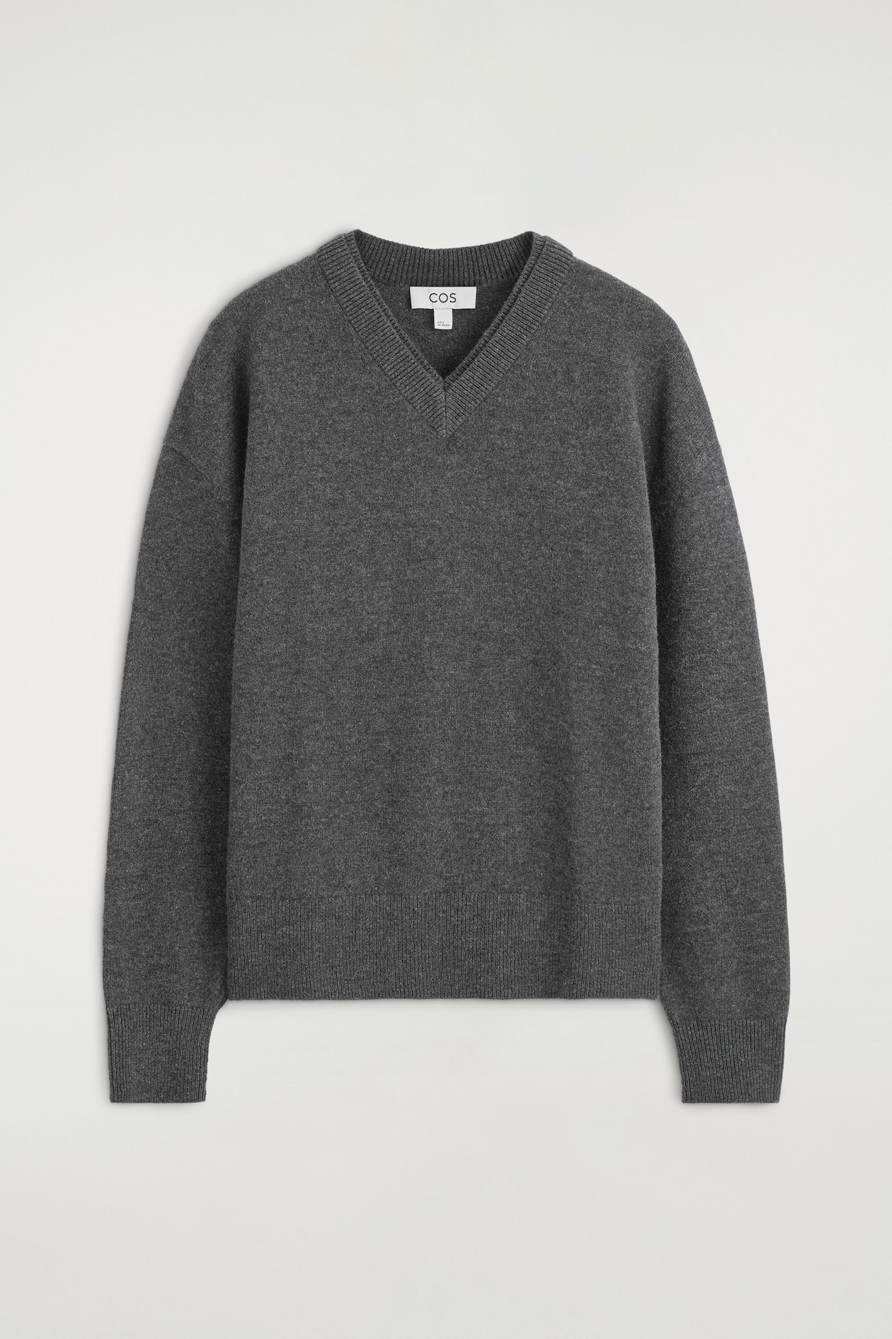 The Merino wool layered V-neck sweater is shown from the front, featuring a double-layered ribbed V-neckline, dropped shoulders, and long sleeves. This dark gray knitwear piece showcases a relaxed silhouette, finished with a ribbed hem and matching ribbed cuffs.