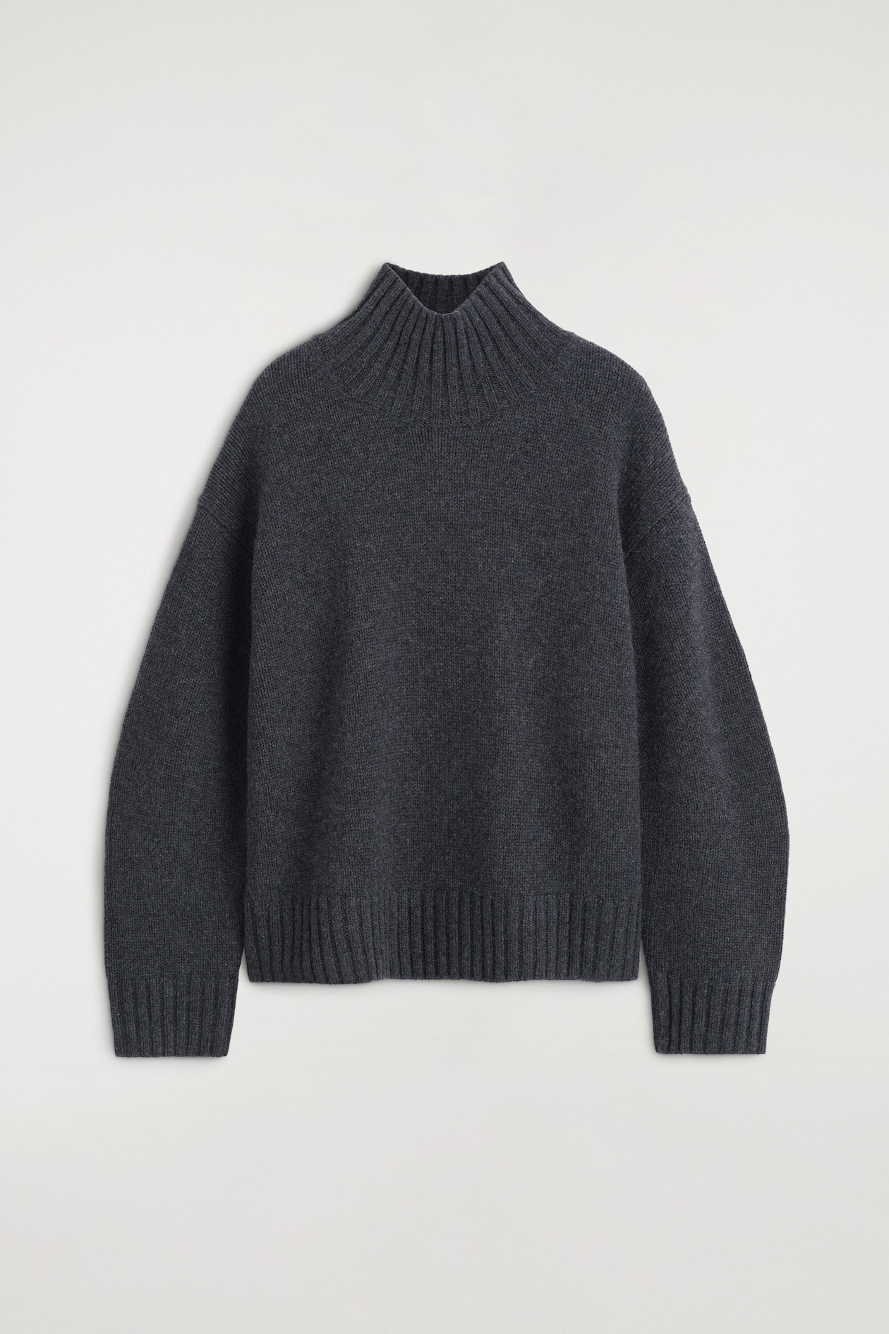 A dark grey chunky cashmere funnel-neck jumper is shown front-facing, showcasing a relaxed fit with dropped shoulders. The jumper features a high ribbed funnel neck, ribbed cuffs, and a matching ribbed hem.