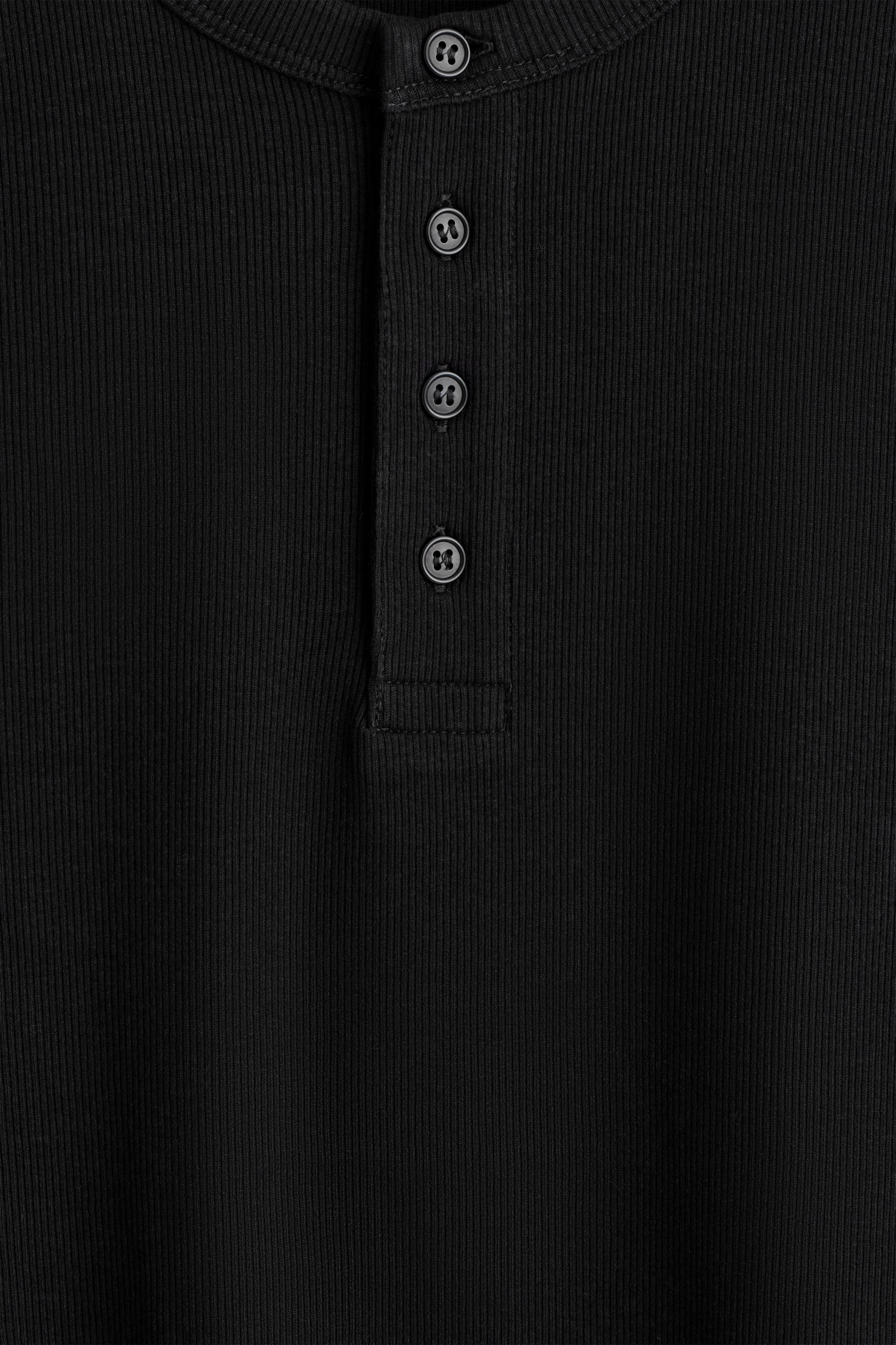 Agrandir l'image: Un t-shirt Henley noir présente sa vue de FACE, avec une texture finement côtelée sur toute sa surface. Une patte de boutonnage à quatre boutons descend au centre du devant, chaque bouton noir affichant un motif subtil en creux.