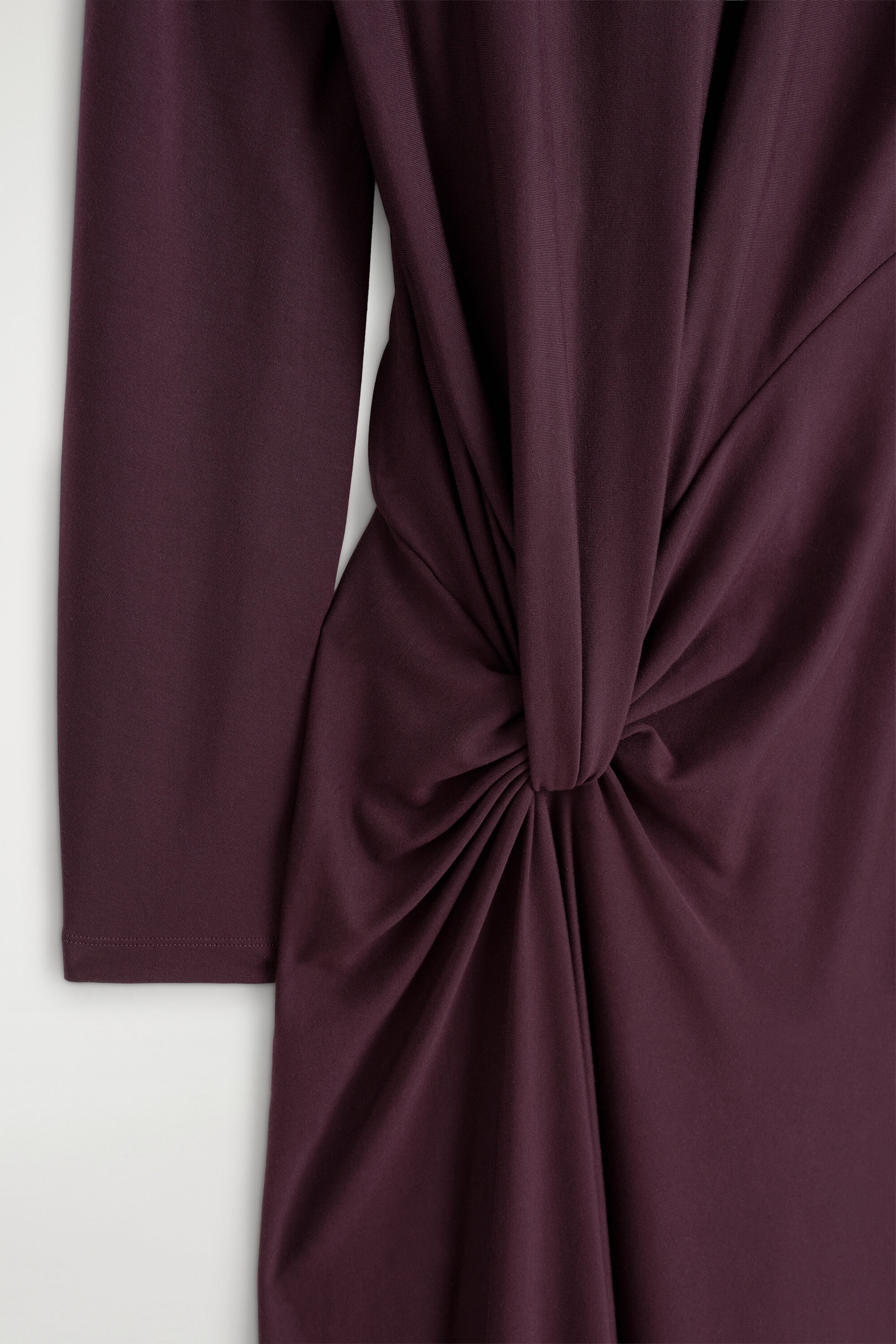 La robe midi plum foncé à détail torsadé et drapé est présentée en gros plan de face, mettant en valeur un nœud torsadé au centre à la taille, qui crée des drapés et des fronces rayonnants. Une manche longue descend sur le côté gauche, mettant en valeur la texture lisse et mate du tissu. La robe midi plum foncé à détail torsadé et drapé est présentée en gros plan de face, mettant en valeur un nœud torsadé au centre à la taille, qui crée des drapés et des fronces rayonnants. Une manche longue descend sur le côté gauche, mettant en valeur la texture lisse et mate du tissu.