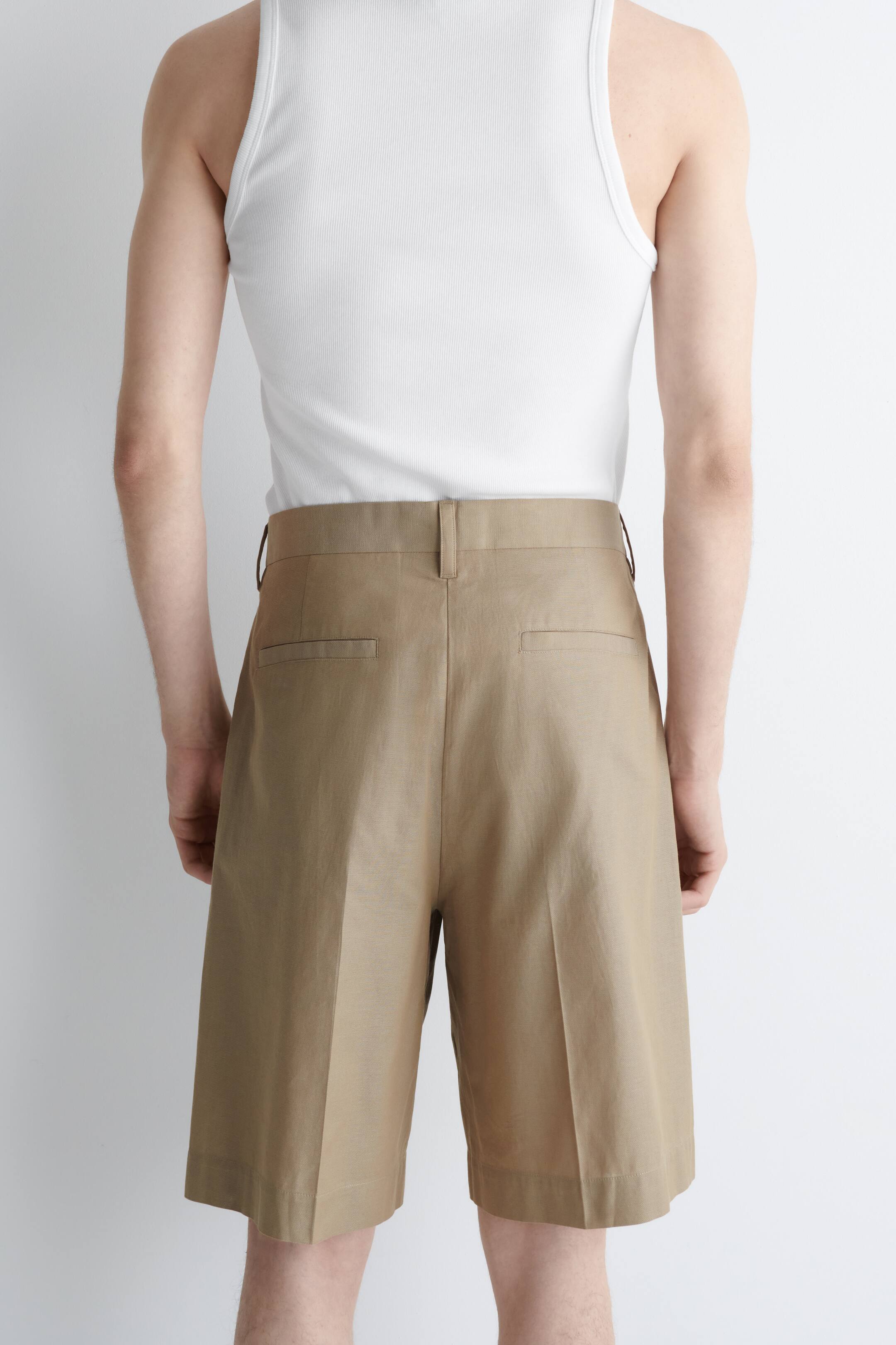 Visualizza immagine più grande: I pantaloncini color cachi sono presentati dal retro, caratterizzati da una vestibilità a vita alta con passanti per cintura e due tasche posteriori a filetto orizzontali, mentre il design a gamba larga si estende appena sopra il ginocchio con pieghe stirate.
