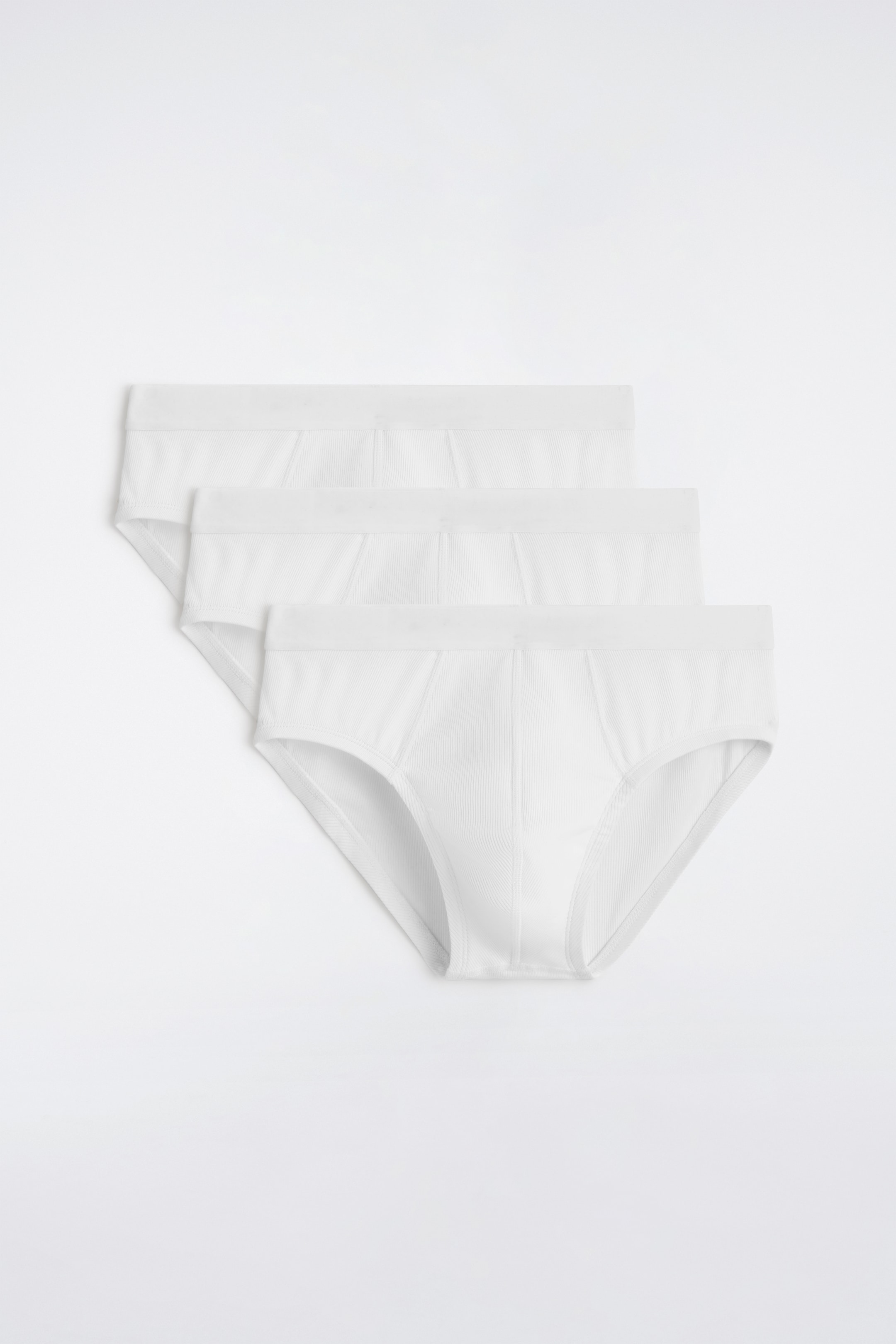 Agrandir l'image: Trois slips blancs côtelés se chevauchent en diagonale, présentés de face. Chaque slip présente une ceinture élastiquée visible et une poche avant distincte, délimitée par des coutures verticales.