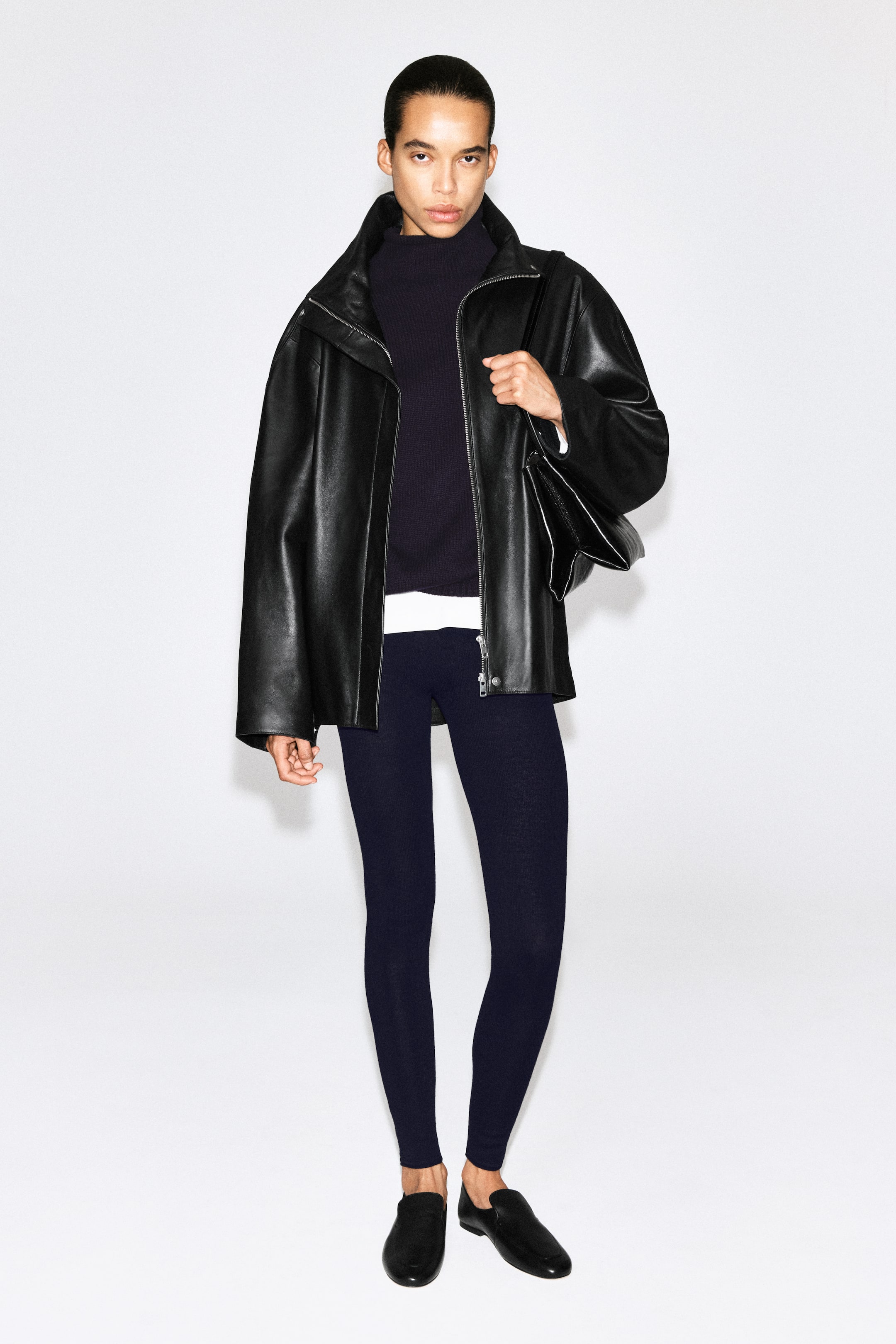Visa större bild: Sömlösa leggings i merinoull i mörk marinblå visas framifrån, med en nära, figurnära silhuett som går ner till anklarna. Leggingsen stylas med en mörk stickad topp, ett vitt underlager som skymtar i midjan, en svart läderjacka och svarta läderslipskor.