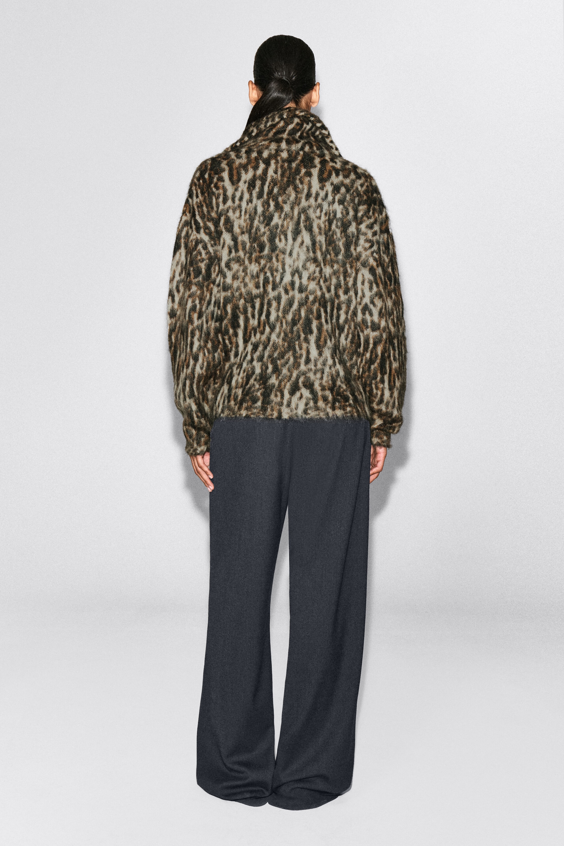 A leopard-patterned mohair-blend jumper is shown from the back, featuring a fuzzy, brushed texture and a high funnel collar. The jumper is styled with dark, wide-leg trousers, highlighting its regular fit and straight hem. A leopard-patterned mohair-blend jumper is shown from the back, featuring a fuzzy, brushed texture and a high funnel collar. The jumper is styled with dark, wide-leg trousers, highlighting its regular fit and straight hem.