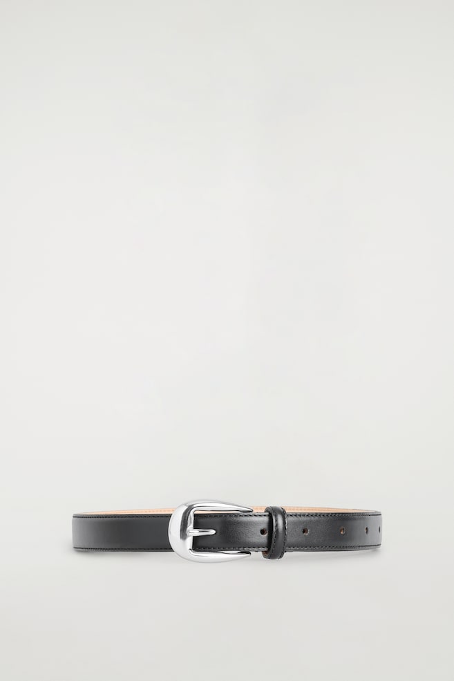 Une ceinture western en cuir, vue de face, présente une lanière en cuir noir lisse avec des surpiqûres ton sur ton sur les bords et une doublure beige clair. Elle se ferme avec une boucle métallique incurvée, polie, de tonalité argentée, accompagnée dâun passant en cuir assorti. - 1