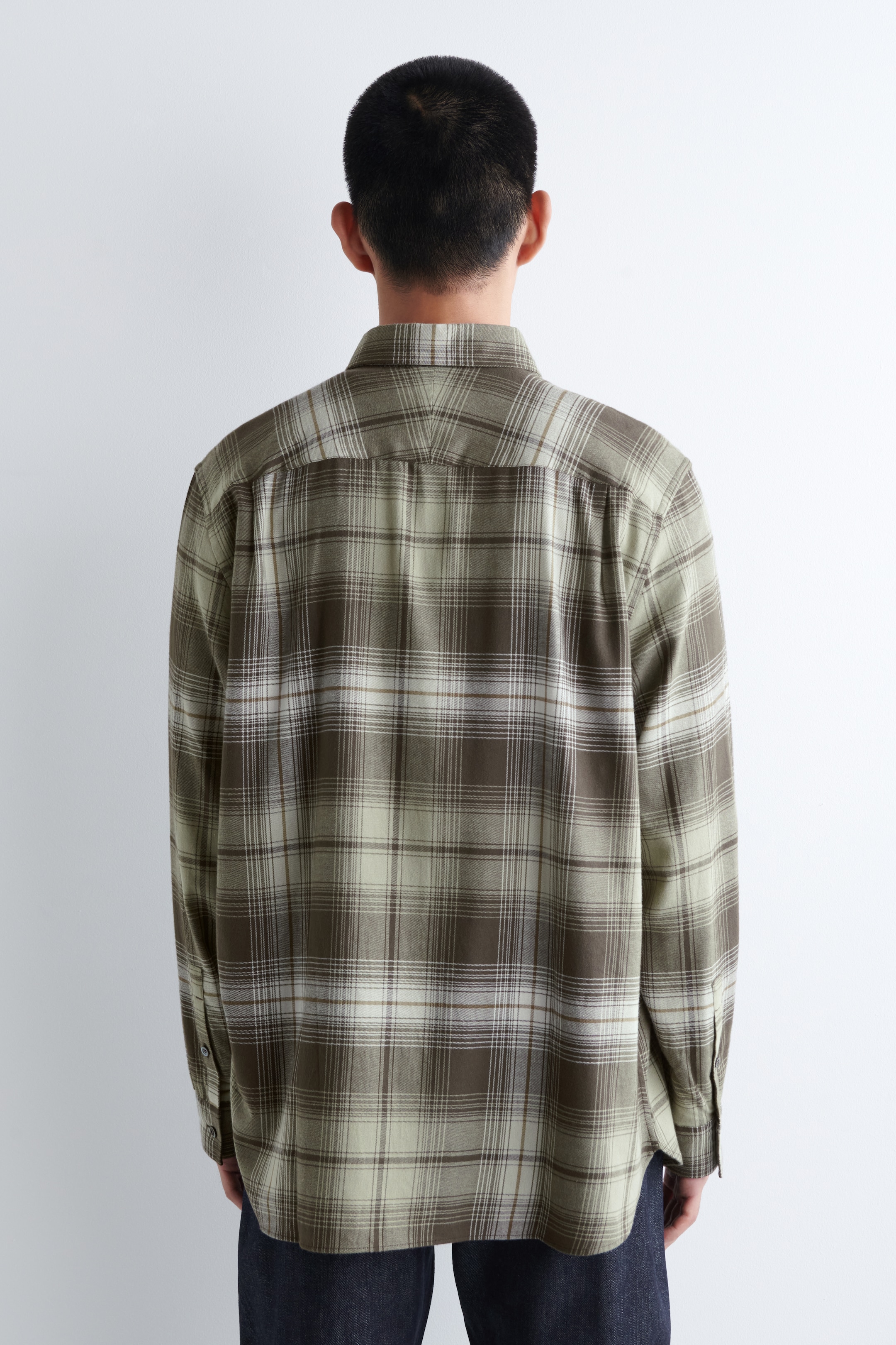 Ver imagen más grande: Se muestra una camisa de manga larga desde atrás, con un patrón de cuadros en verde, marrón y blanco. Está diseñada con un canesú visible en la espalda y mangas largas que terminan en puños abotonados, presentando un ajuste relajado.