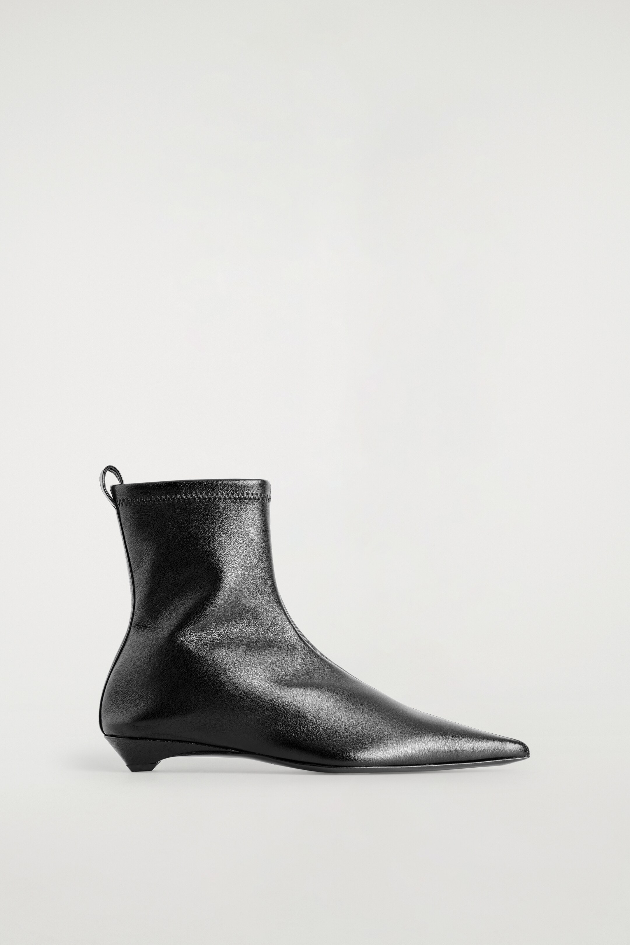 Größeres Bild ansehen: Ein schwarzer, spitzer Leder-Sockenstiefel wird angezeigt, nach rechts gerichtet. Er präsentiert ein glattes Lederobermaterial, das zu einer spitzen Zehenpartie führt, und einen eng anliegenden, sockenartigen Knöchelschaft, der mit einem genähten elastischen Bündchen und einer kleinen Zuglasche hinten abgeschlossen ist. Ein niedriger, konisch zulaufender Absatz stützt den Stiefel.