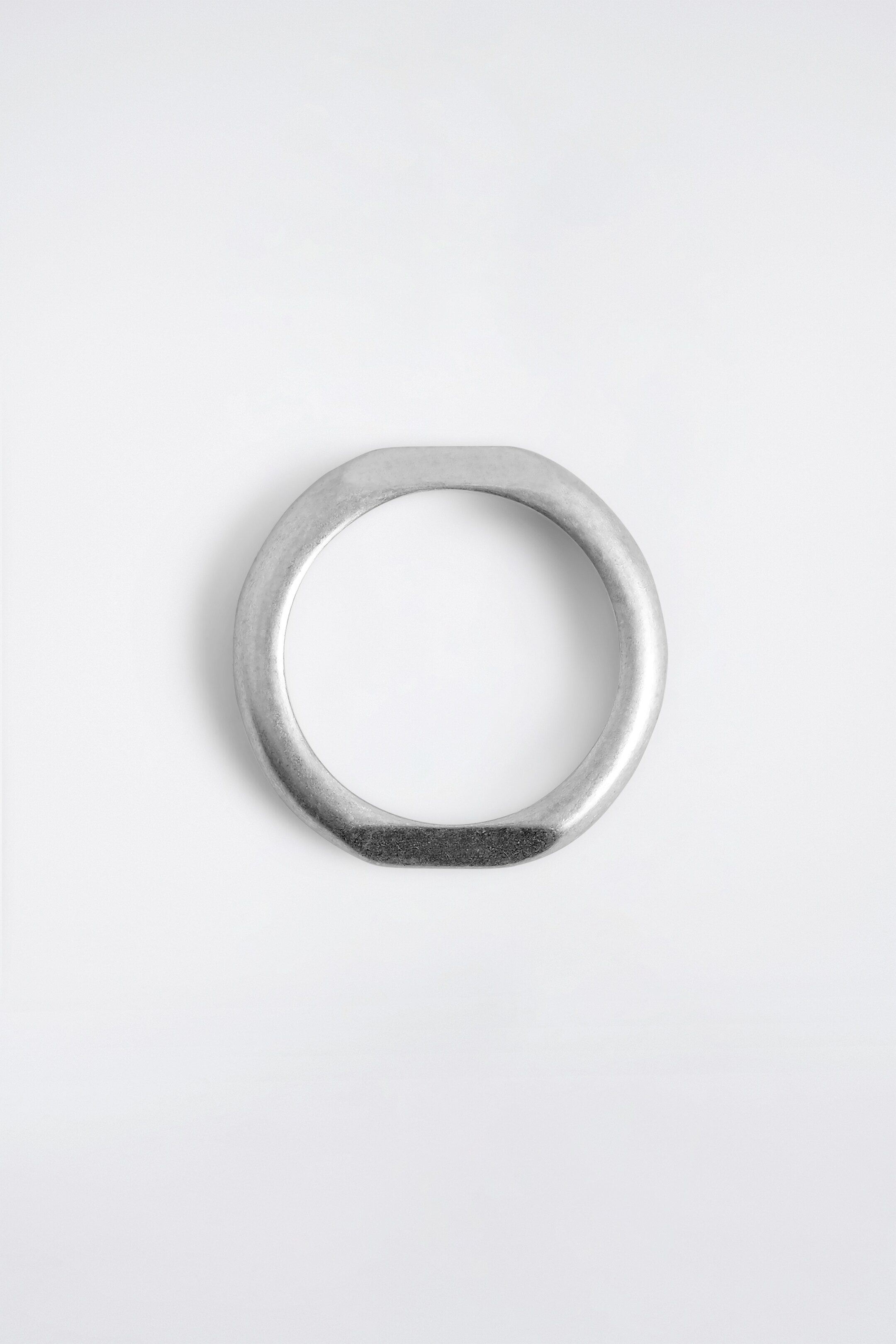 Agrandir l'image: Une bague de ton argenté est posée à plat, vue d'un angle supérieur. Elle présente une forme circulaire avec des sections aplaties distinctes en haut et en bas, la section inférieure présentant une finition sombre et texturée contrastante.