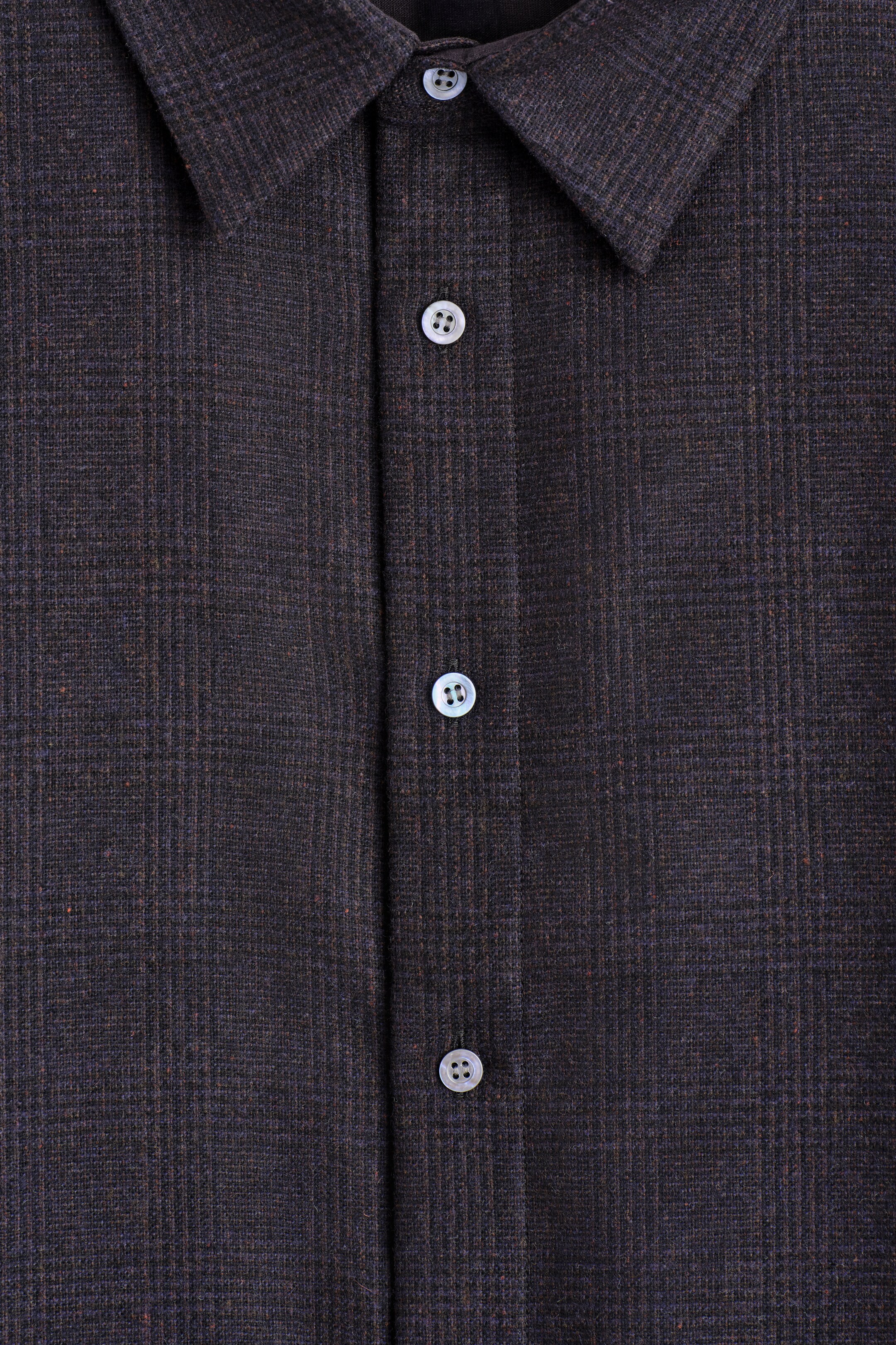 View larger image: A dark, textured shirt is being shown FRONT, featuring a subtle check pattern. It is designed with a pointed collar, and light, iridescent buttons are fastening its central placket.