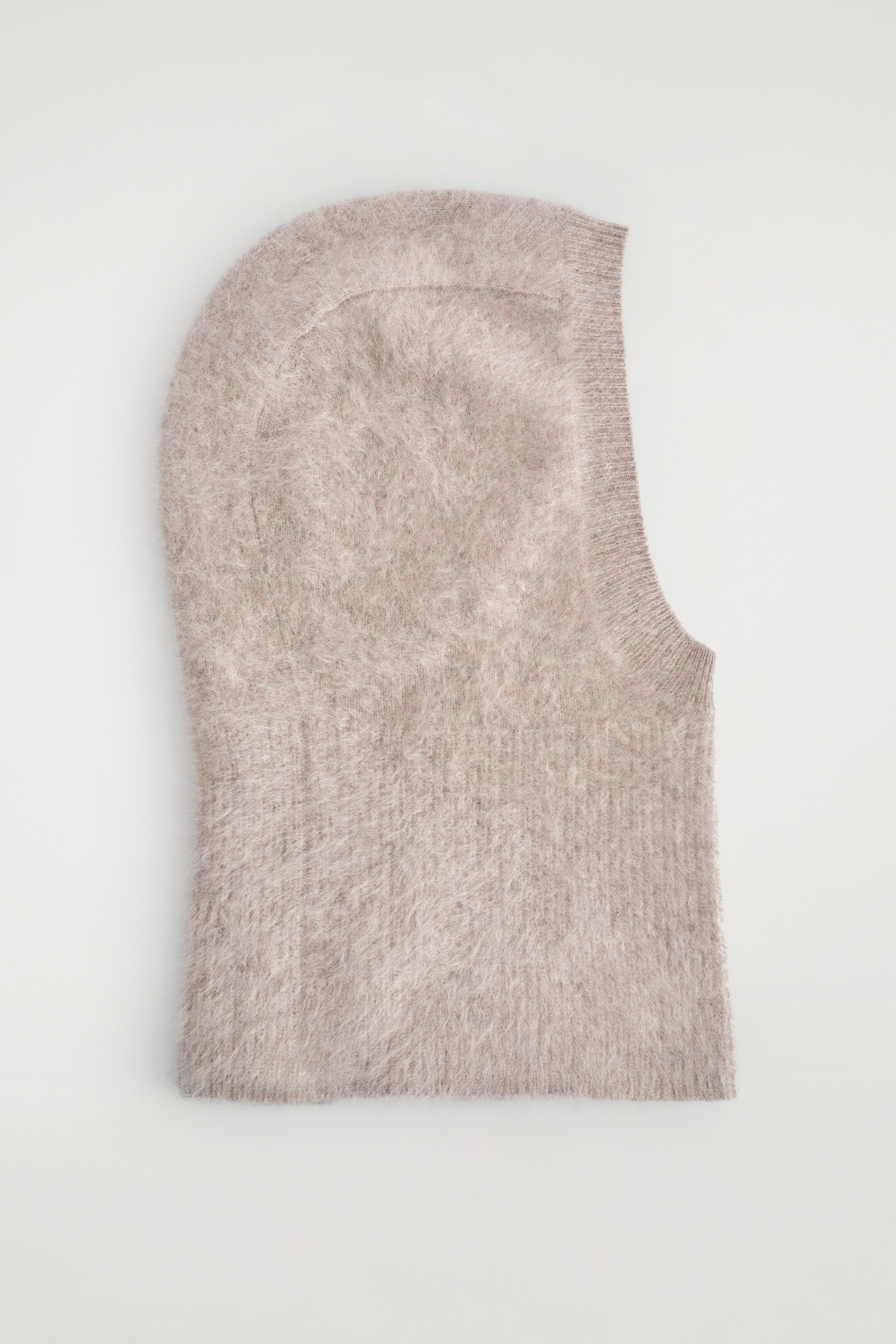 View larger image: A light beige balaclava is lying flat, displaying a fluffy knit texture and featuring a rounded top, a straight bottom edge, and a vertical face opening on the right.