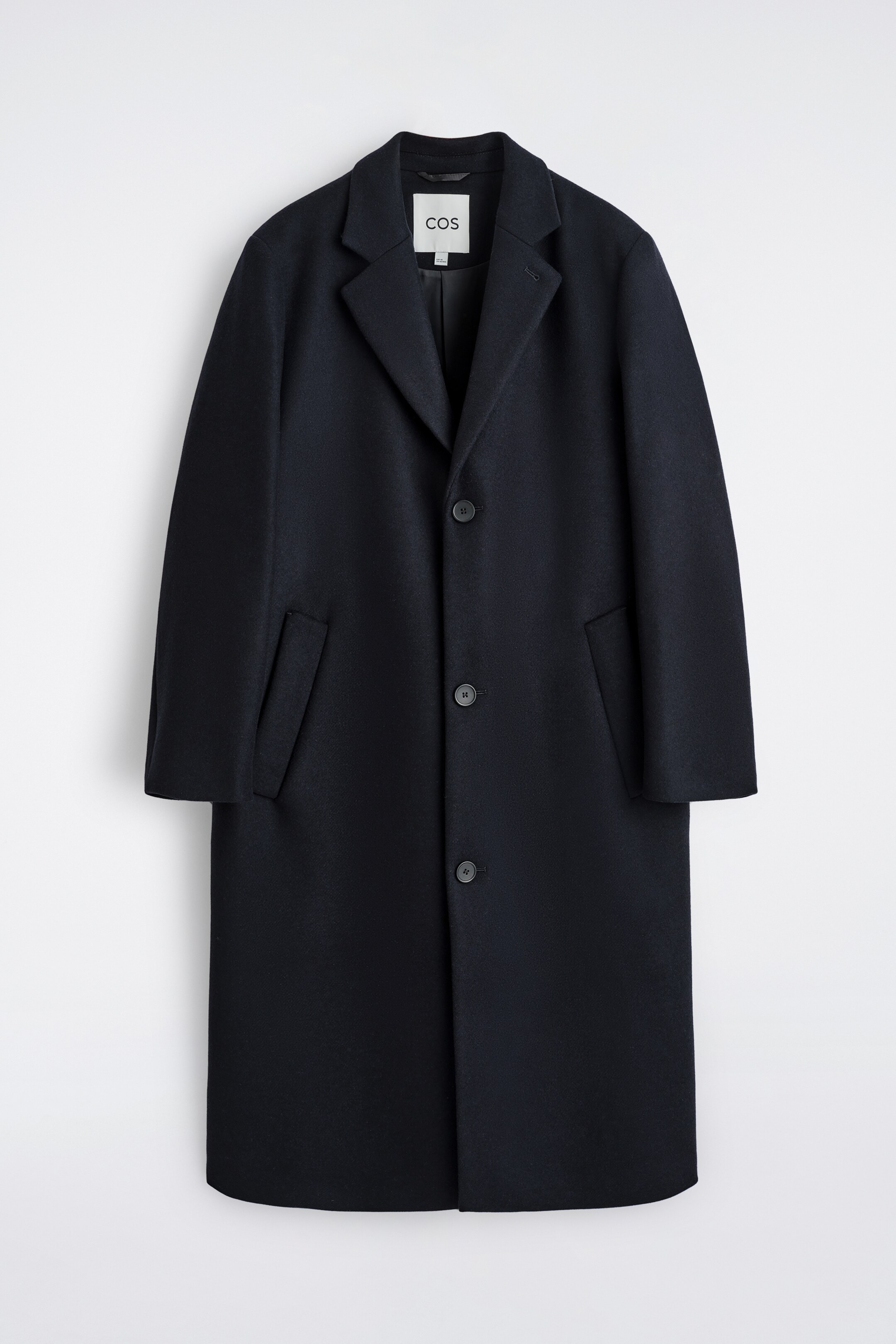 View larger image: A dark blue, single-breasted coat is presenting its front, featuring a relaxed fit, classic notch lapels, and a three-button closure. Two welt pockets are visible at the hips.