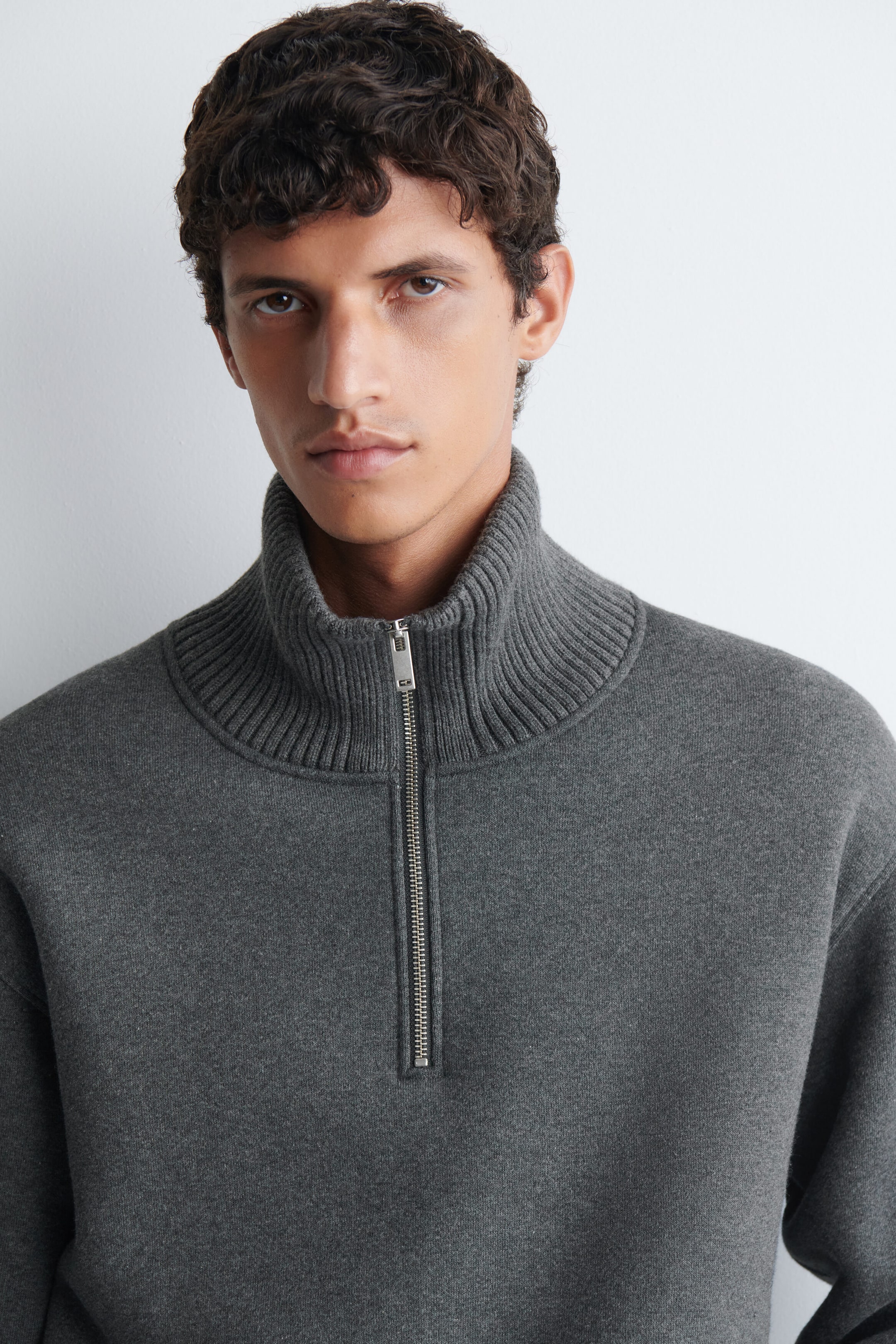 A dark grey cotton-blend jersey zip-up sweater is being worn by the model, featuring a high ribbed collar and a silver metal half-zip closure. A dark grey cotton-blend jersey zip-up sweater is being worn by the model, featuring a high ribbed collar and a silver metal half-zip closure.