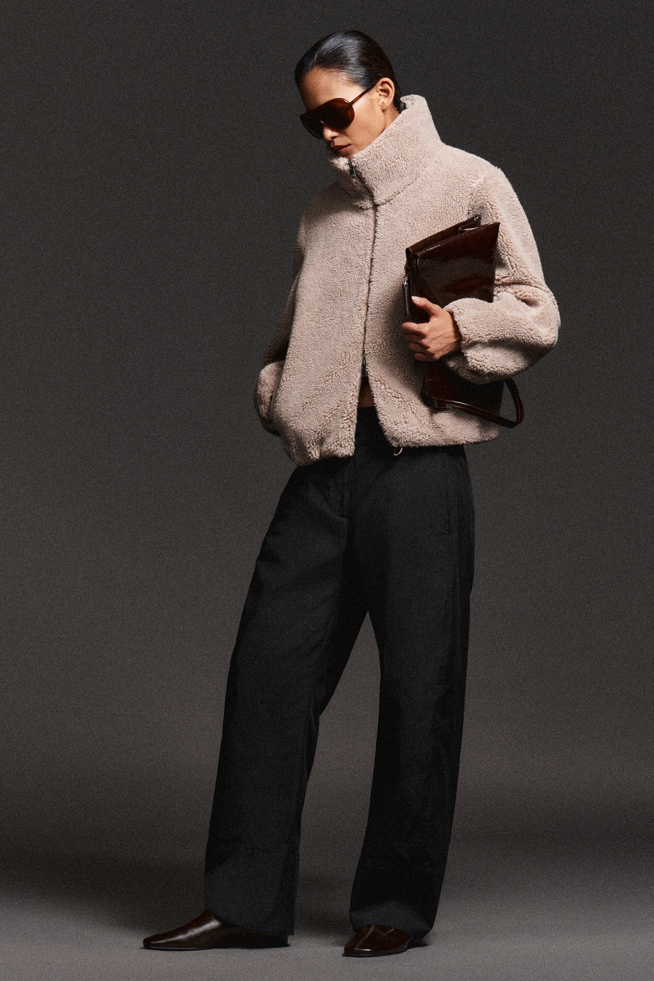 A beige, textured fleece jacket featuring a high funnel neck and a two-way zip closure is shown from the front on a model. The jacket is styled with wide-leg black trousers, highlighting its soft, wool-like texture, regular fit, and side pockets. A beige, textured fleece jacket featuring a high funnel neck and a two-way zip closure is shown from the front on a model. The jacket is styled with wide-leg black trousers, highlighting its soft, wool-like texture, regular fit, and side pockets.