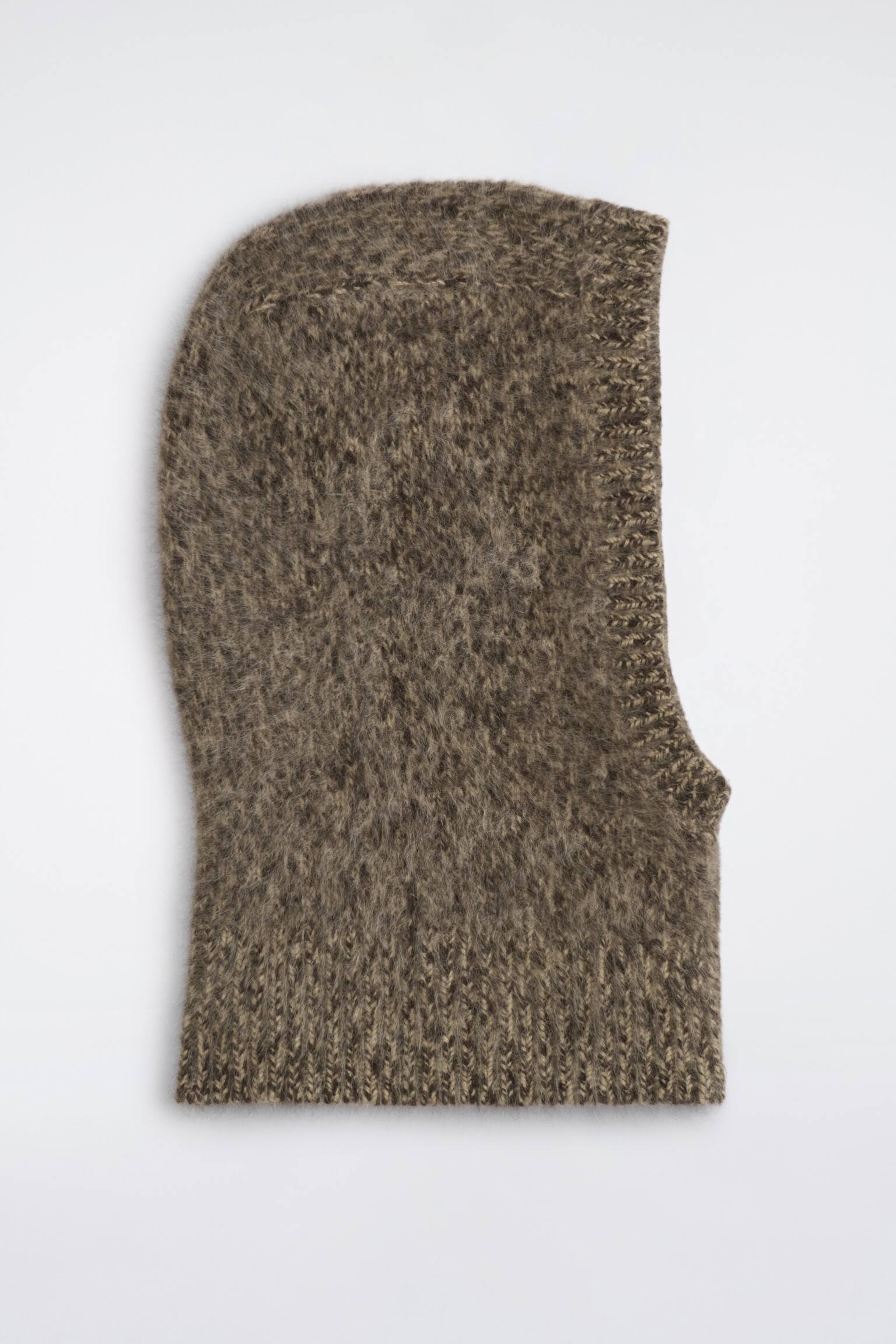 Una balaclava de cachemira cepillada en punto marrÃ³n jaspeado aparece tendida en posiciÃ³n horizontal, vista de perfil lateral, mostrando su superficie suave y texturizada. Presenta un acabado acanalado alrededor de la abertura para el rostro y un amplio bajo acanalado en el cuello.