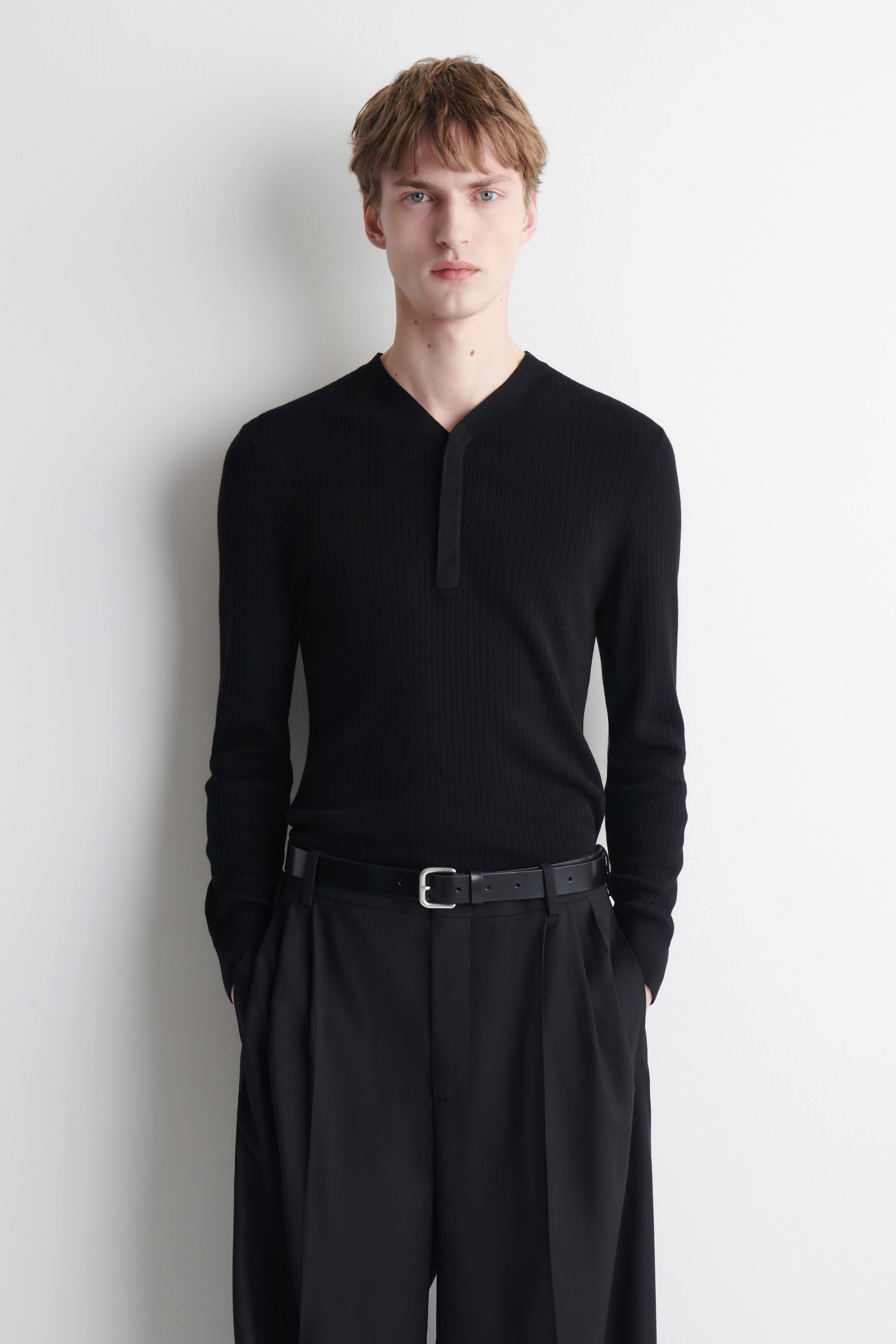 View larger image: The black long-sleeved top, shown from the front, features a ribbed texture and a V-neckline with a short placket displaying three visible buttons. It fits closely to the body.