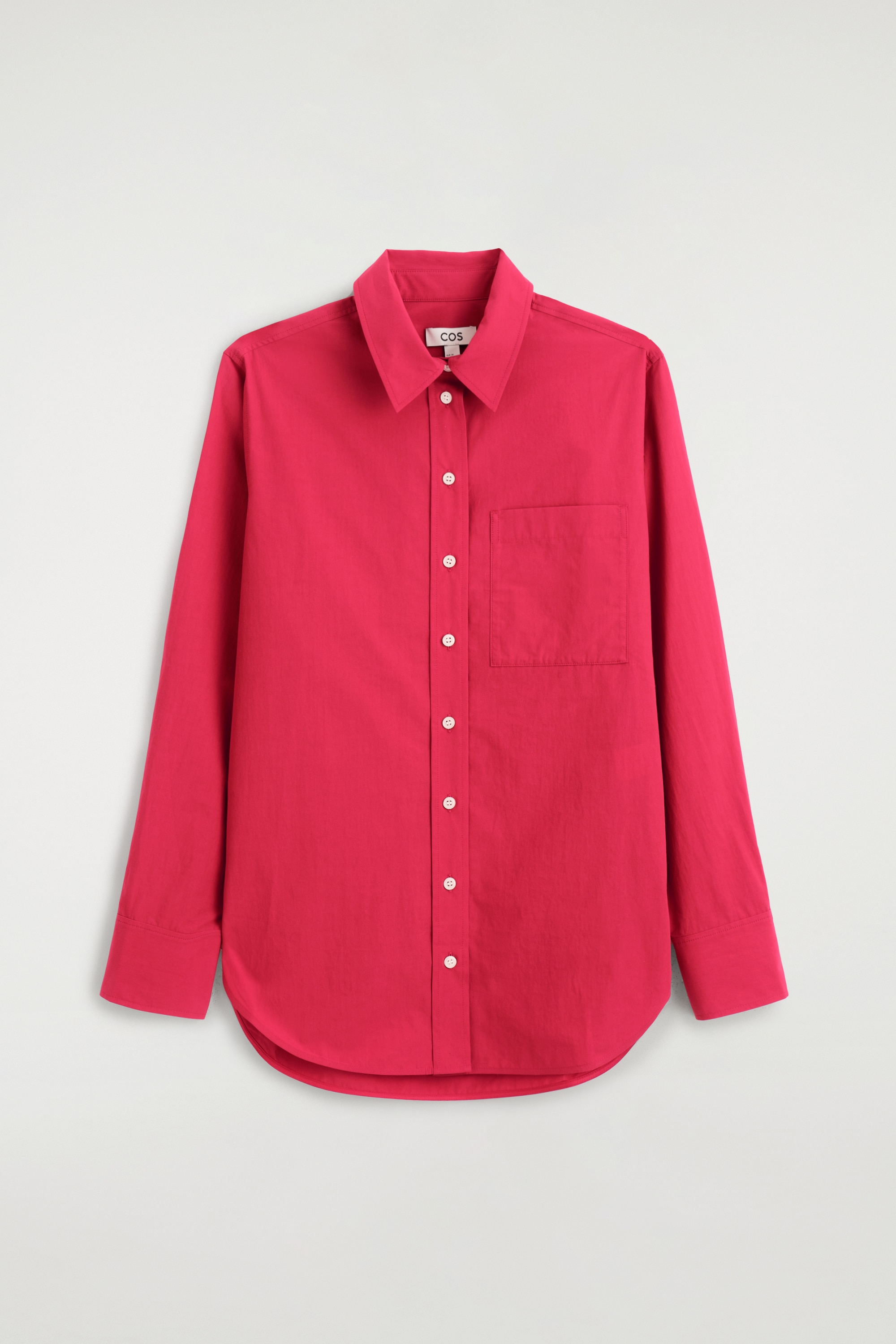Une chemise rouge Ã  manches longues et boutonnÃ©e est portÃ©e par le mannequin, rentrÃ©e dans un pantalon foncÃ© avec une ceinture noire. La chemise prÃ©sente des boutons blancs sur le devant, un col pointu et se porte avec les premiers boutons laissÃ©s ouverts.