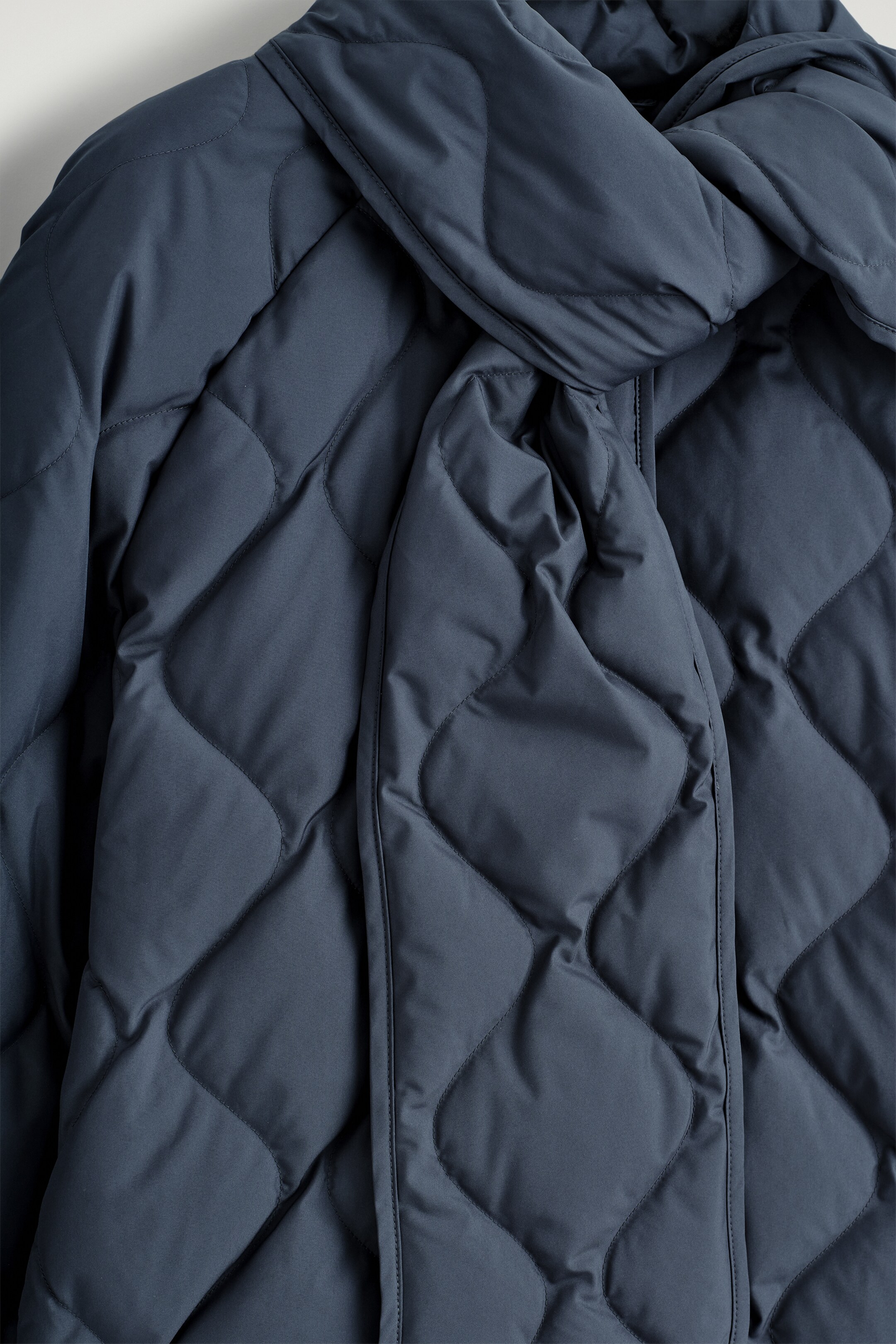 View larger image: A navy quilted jacket is presenting a diamond quilting pattern across its surface. A matching tonal scarf is wrapped around the neck area.