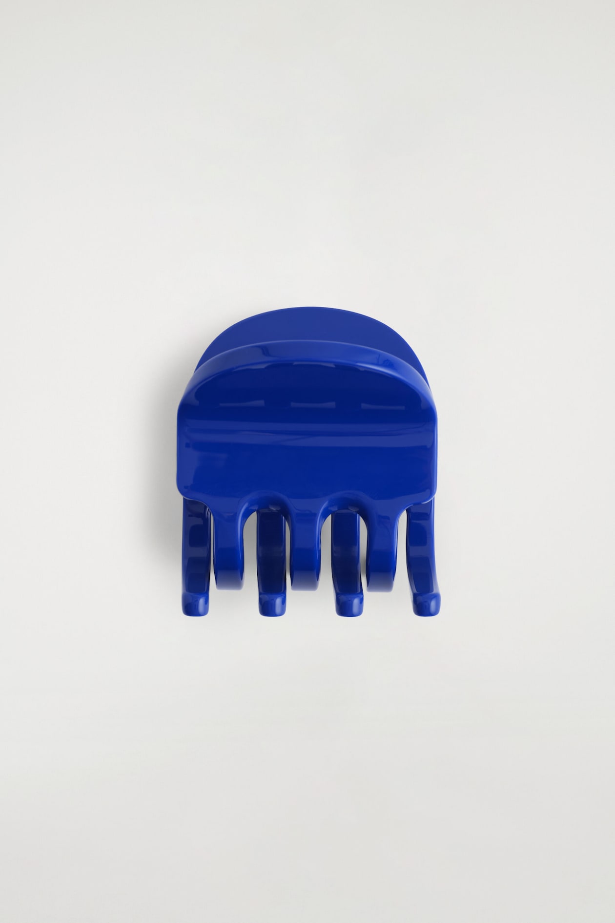 A glossy, cobalt blue hair claw clip is facing front, featuring a rounded top handle and thick, curved claws pointing downward.