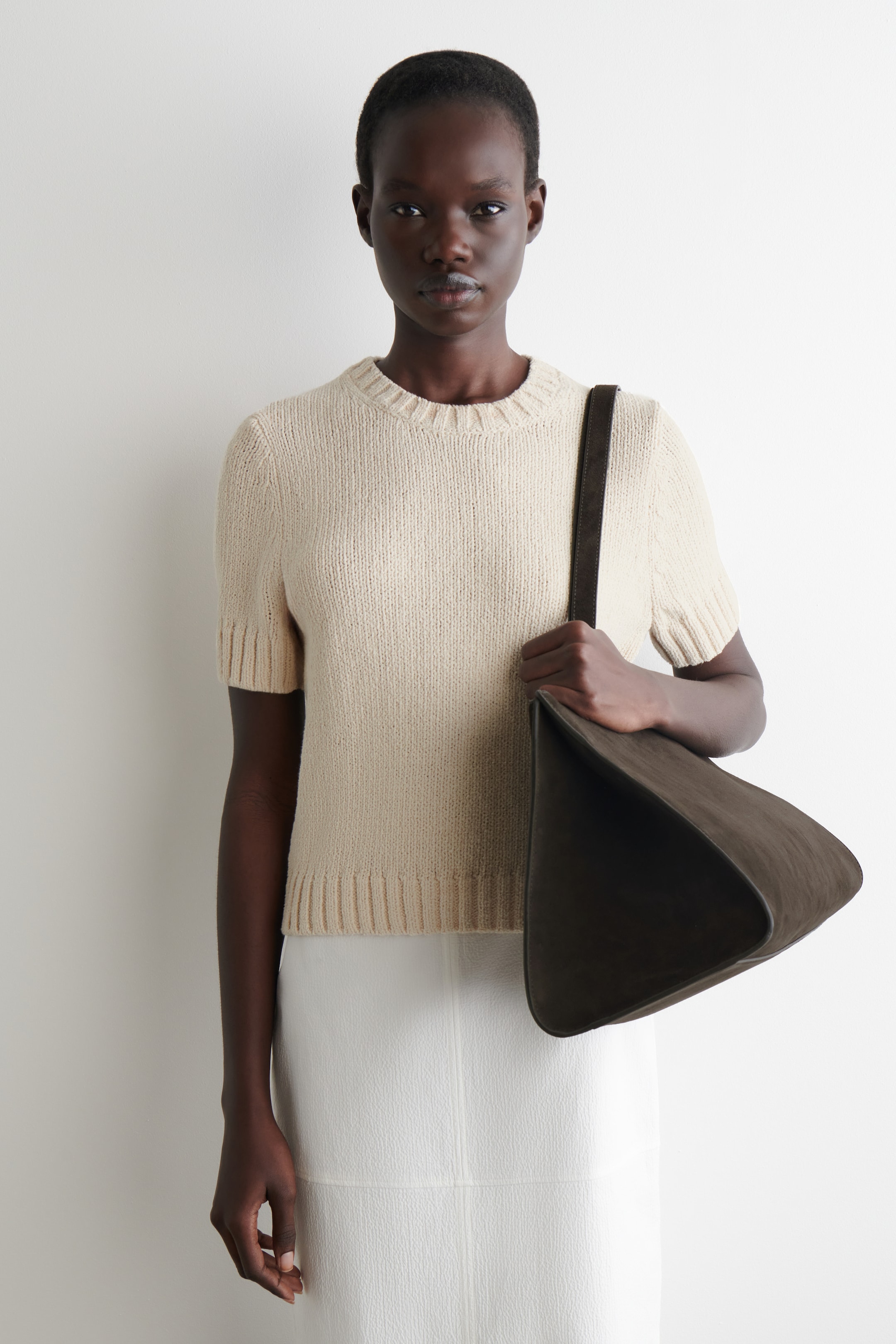 View larger image: A light beige knitted short-sleeved top is being worn, featuring a crew neck with a ribbed collar, short sleeves with ribbed cuffs, and a ribbed hem. It is presenting a regular fit and a slightly cropped length.
