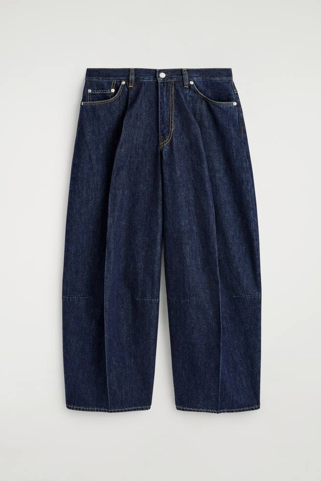 Un pantalon en jean bleu foncé à jambes droites est présenté de FACE, avec des plis marqués pliés descendant le long de l'avant des jambes. Le jean est conçu avec une ceinture, des passants de ceinture, une fermeture à bouton et à zip, des poches avant incurvées, et des détails de coutures horizontales distinctes sur les panneaux inférieurs des jambes, le tout accentué par des surpiqûres contrastées jaunes. - 1