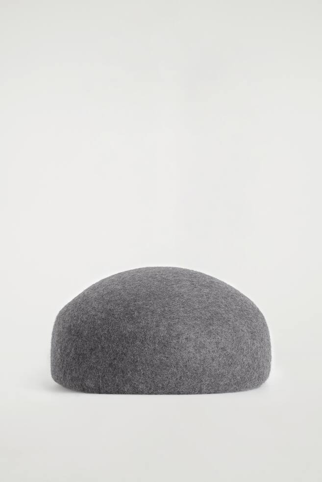 The sculpted wool beret showcases a structured, rounded dome silhouette in textured medium grey wool felt. It is resting flat and facing front, highlighting its seamless, minimalist design and clean edges. - 1