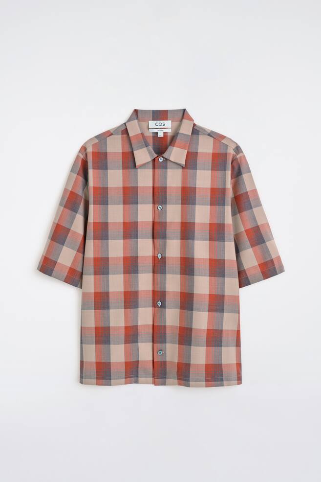 Une chemise Ã  manches courtes prÃ©sente un motif Ã  carreaux beige, orange rougeÃ¢tre et bleu-gris. Elle est dotÃ©e dâun col pointu et dâune fermeture boutonnÃ©e sur toute la longueur avec des boutons de couleur claire, montrÃ©e de face. - 1