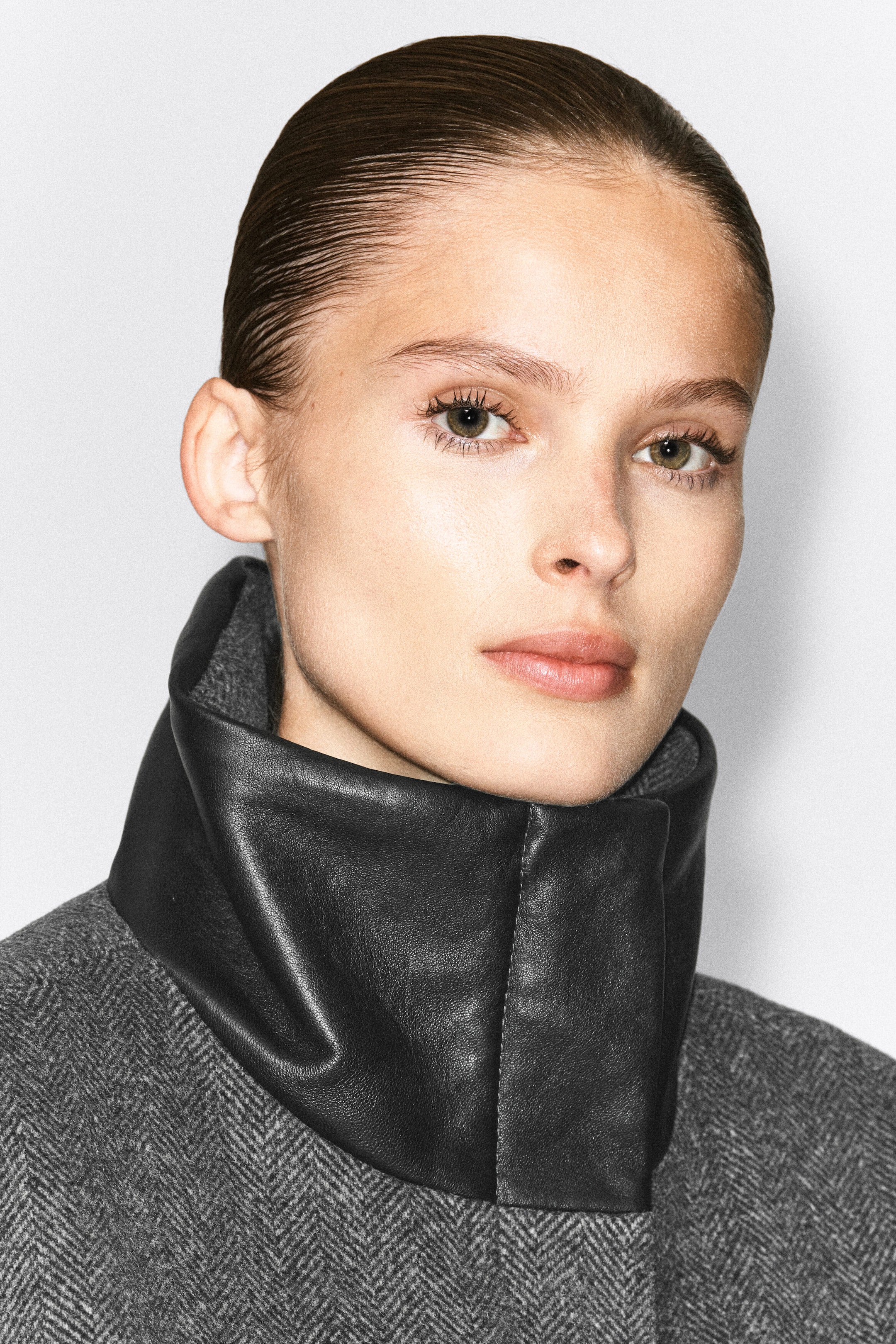 Das Model trägt eine graue Jacke aus Wollmischung in Fischgrätmuster mit hohem, schwarzem Leder-Funnel-Ausschnitt. Die Nahaufnahme betont den Kontrast zwischen dem strukturierten Lederkragen und dem gemusterten Wollstoff. Das Model trägt eine graue Jacke aus Wollmischung in Fischgrätmuster mit hohem, schwarzem Leder-Funnel-Ausschnitt. Die Nahaufnahme betont den Kontrast zwischen dem strukturierten Lederkragen und dem gemusterten Wollstoff.
