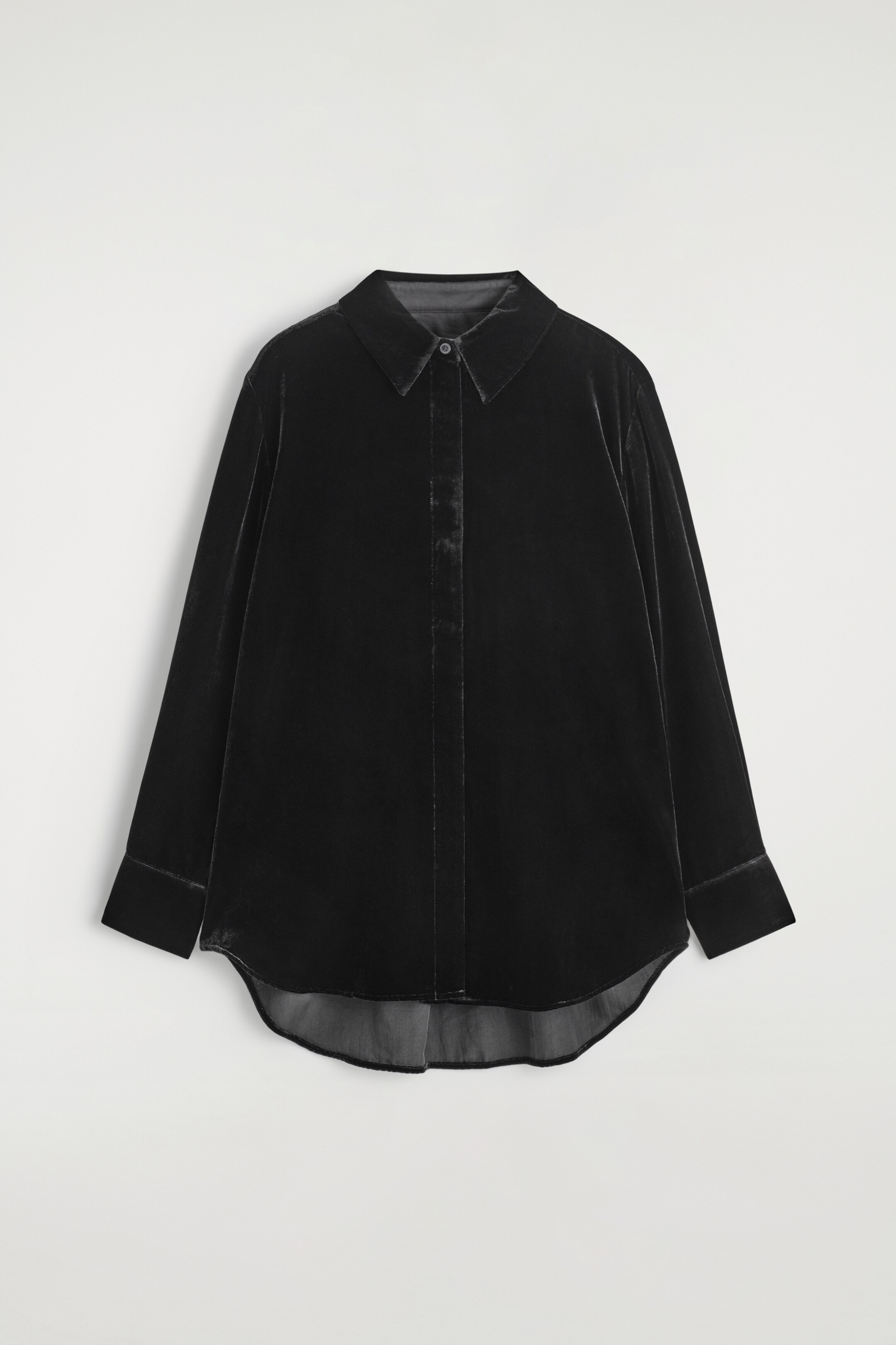 Visualizza immagine più grande: Una camicia in velluto scuro viene presentata dal davanti, caratterizzata da una silhouette rilassata. Presenta un colletto a punta, un'allacciatura nascosta al centro e maniche lunghe con polsini semplici, con un orlo curvo.