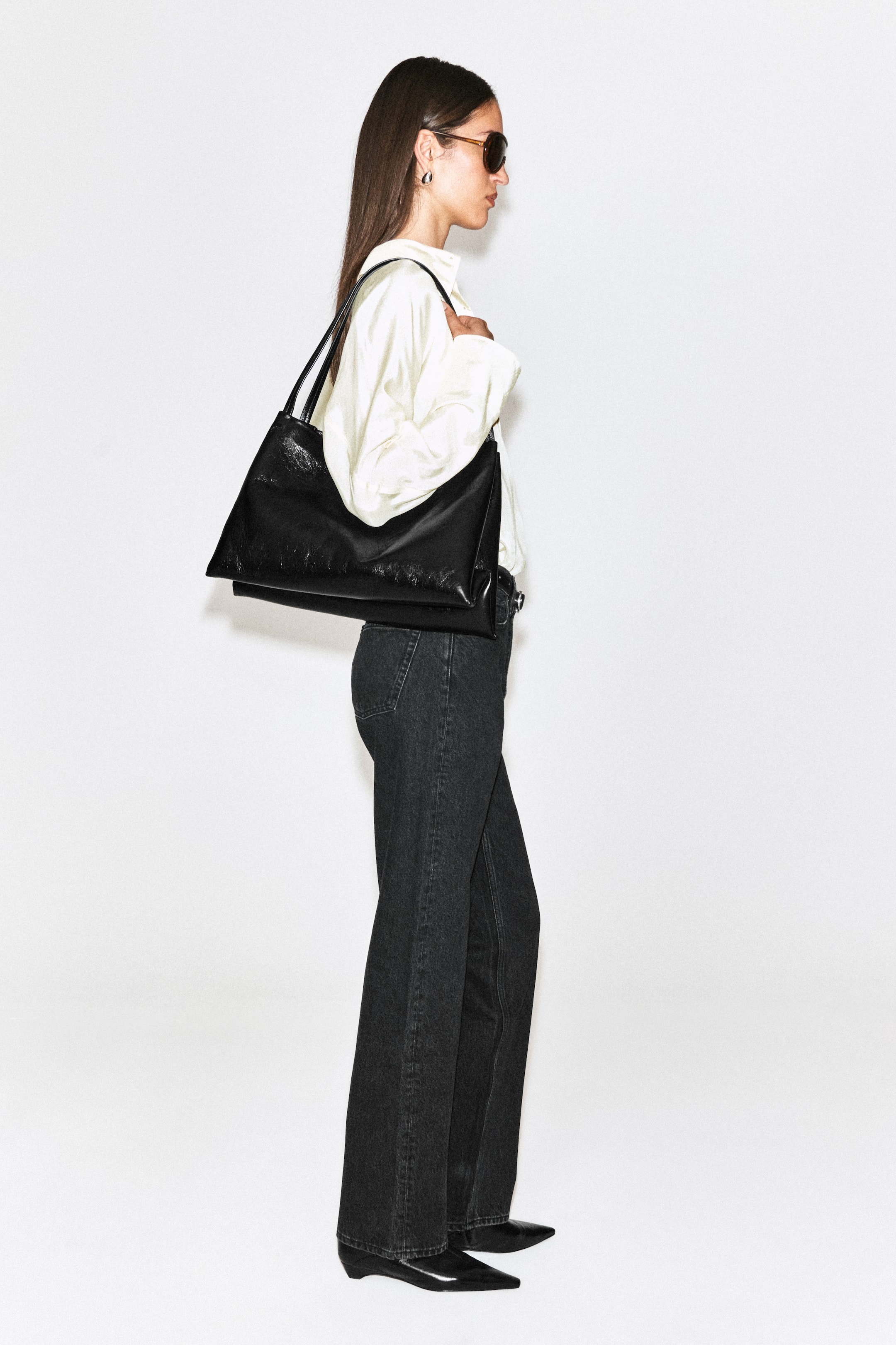 Größeres Bild ansehen: Die Chord Straight-Leg-Jeans in dunkler Denim-Waschung wird vom Model getragen und überzeugt mit High-Waist-Passform sowie einer entspannten, geraden Silhouette. Die Jeans ist mit einem in den Bund gesteckten cremefarbenen Langarmhemd, schwarzen Stiefeletten mit spitzer Spitze und einer schwarzen Leder-Umhängetasche kombiniert.