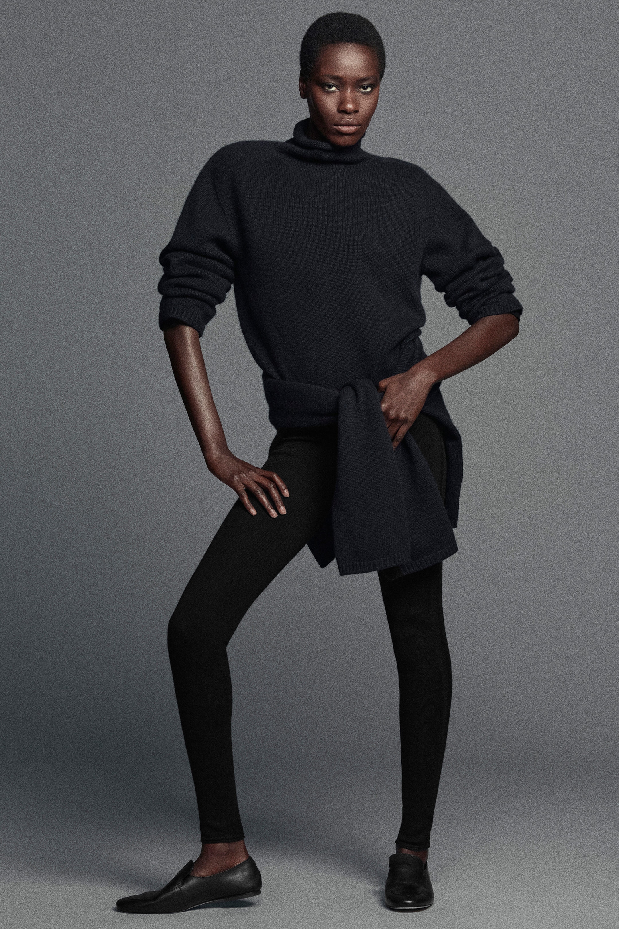 Un mannequin porte un pull en cachemire bleu marine foncé à col montant, présenté de face, avec une coupe décontractée, un col roulé haut et un vêtement en maille assorti noué à la taille. La tenue est complétée par des leggings en laine mérinos noire, près du corps et sans coutures, qui se resserrent à la cheville, associés à des mocassins plats en cuir. Un mannequin porte un pull en cachemire bleu marine foncé à col montant, présenté de face, avec une coupe décontractée, un col roulé haut et un vêtement en maille assorti noué à la taille. La tenue est complétée par des leggings en laine mérinos noire, près du corps et sans coutures, qui se resserrent à la cheville, associés à des mocassins plats en cuir.