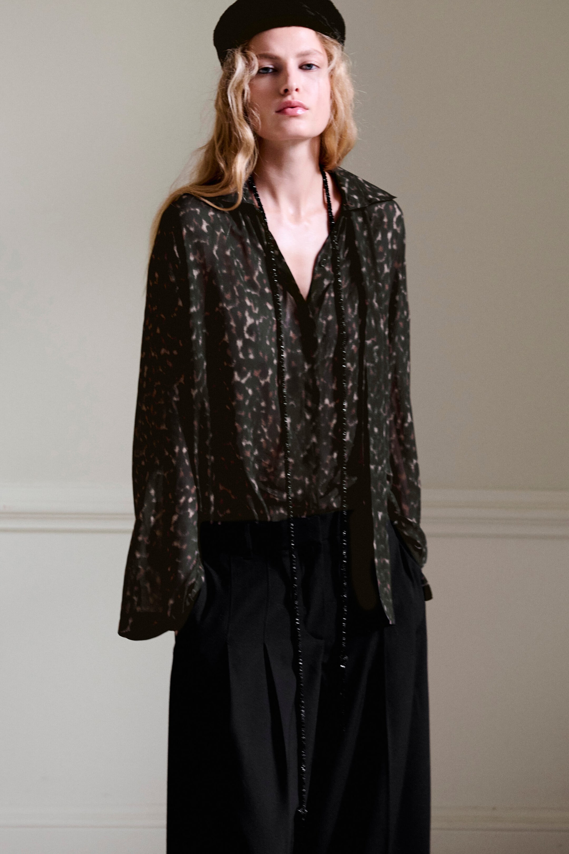 Das Model ist frontal ausgerichtet und trägt ein fließendes Oberteil mit dunklem Leopardenprint und passendem Schaldetail, das in eine hoch taillierte, schwarze, weit geschnittene Hose aus Wollmischung mit Bundfalten gesteckt ist. Das Oberteil verfügt über lange, lockere Ärmel und einen tiefen V-Ausschnitt, während die Hose mit markanten Bundfalten vorne versehen ist, die ihren voluminösen Fall unterstreichen. Das Model ist frontal ausgerichtet und trägt ein fließendes Oberteil mit dunklem Leopardenprint und passendem Schaldetail, das in eine hoch taillierte, schwarze, weit geschnittene Hose aus Wollmischung mit Bundfalten gesteckt ist. Das Oberteil verfügt über lange, lockere Ärmel und einen tiefen V-Ausschnitt, während die Hose mit markanten Bundfalten vorne versehen ist, die ihren voluminösen Fall unterstreichen.